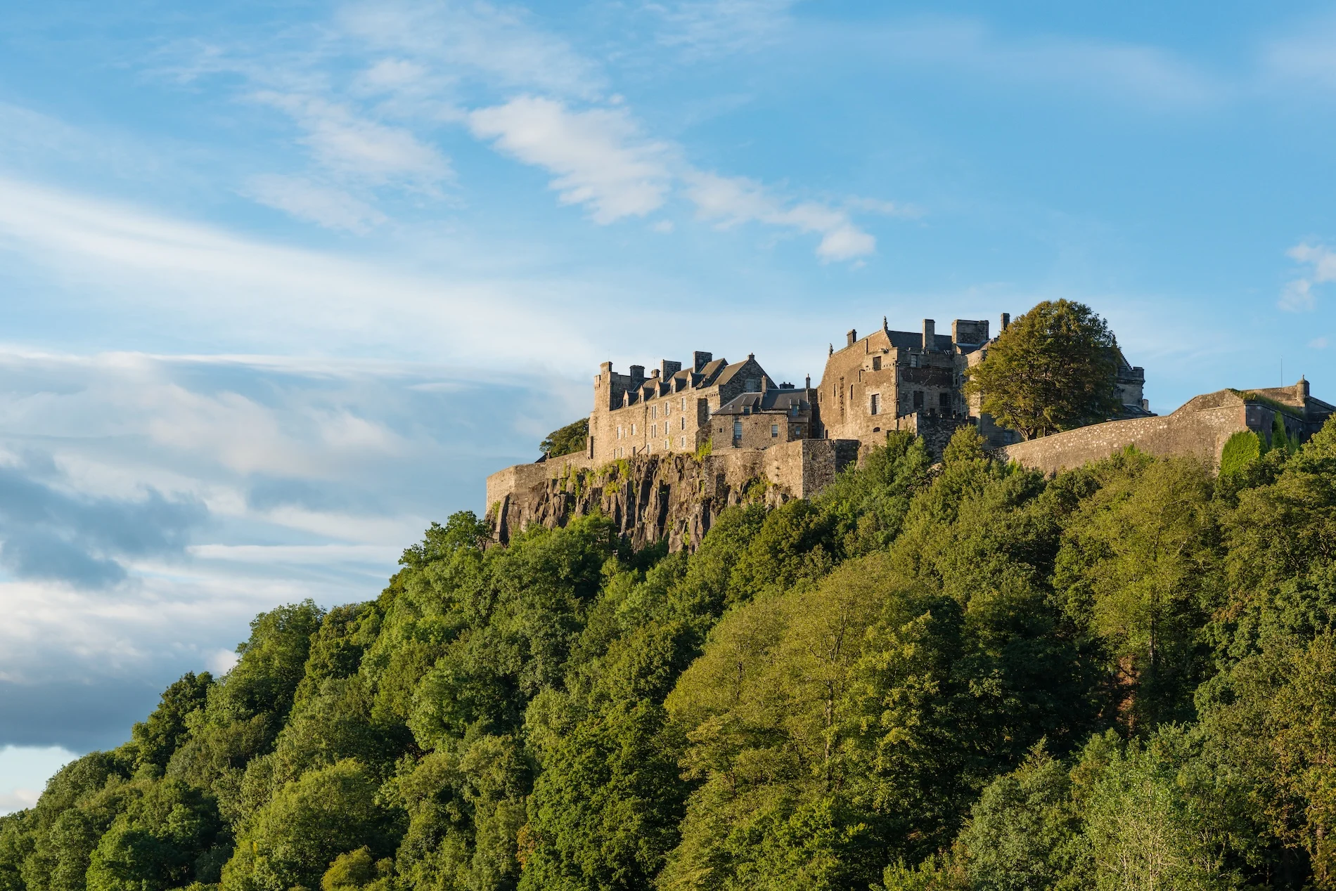 Historic Scottish castle perched on rocky hilltop surrounded by green forest