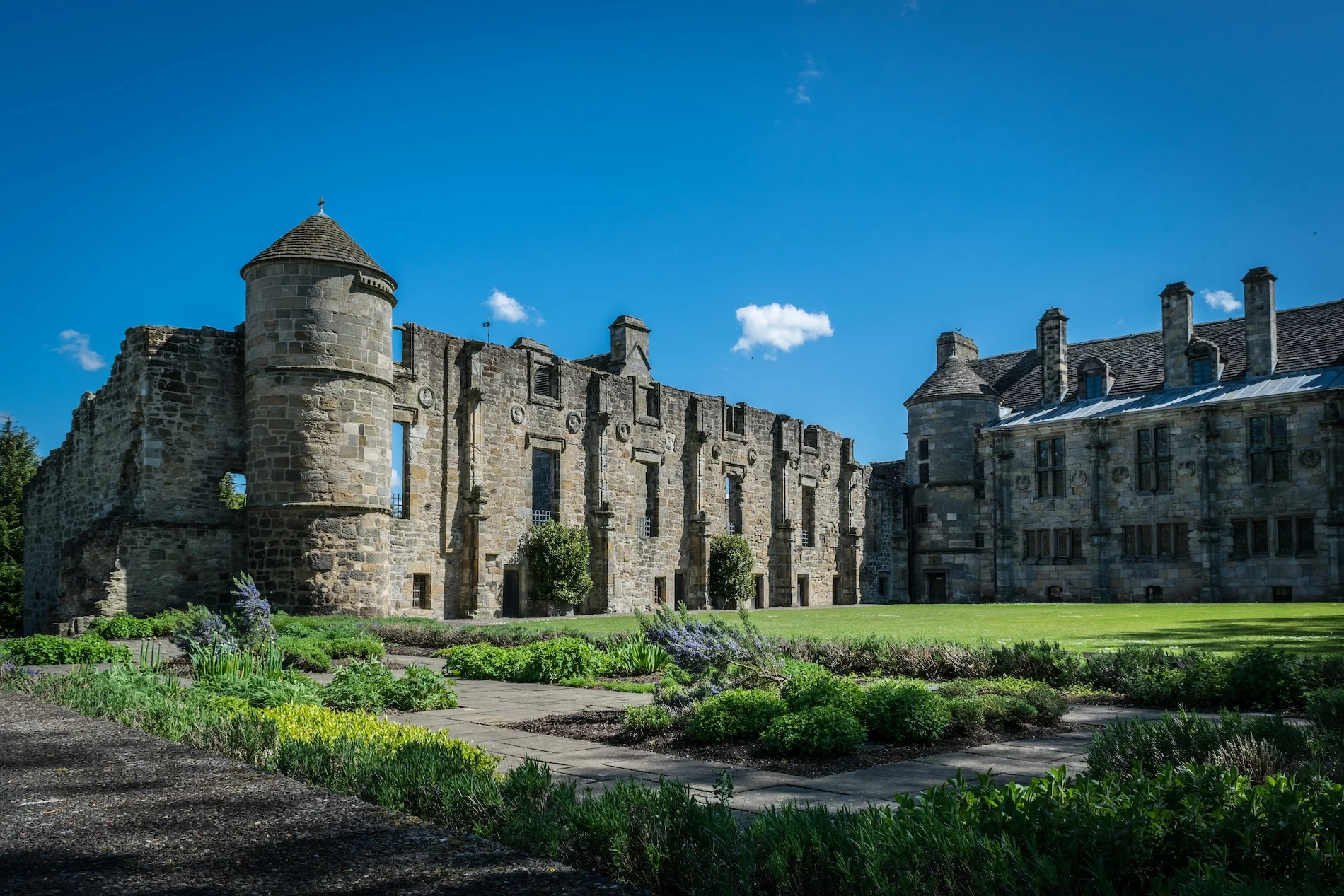 Historic Scottish castle ruins with manicured gardens under blue sky