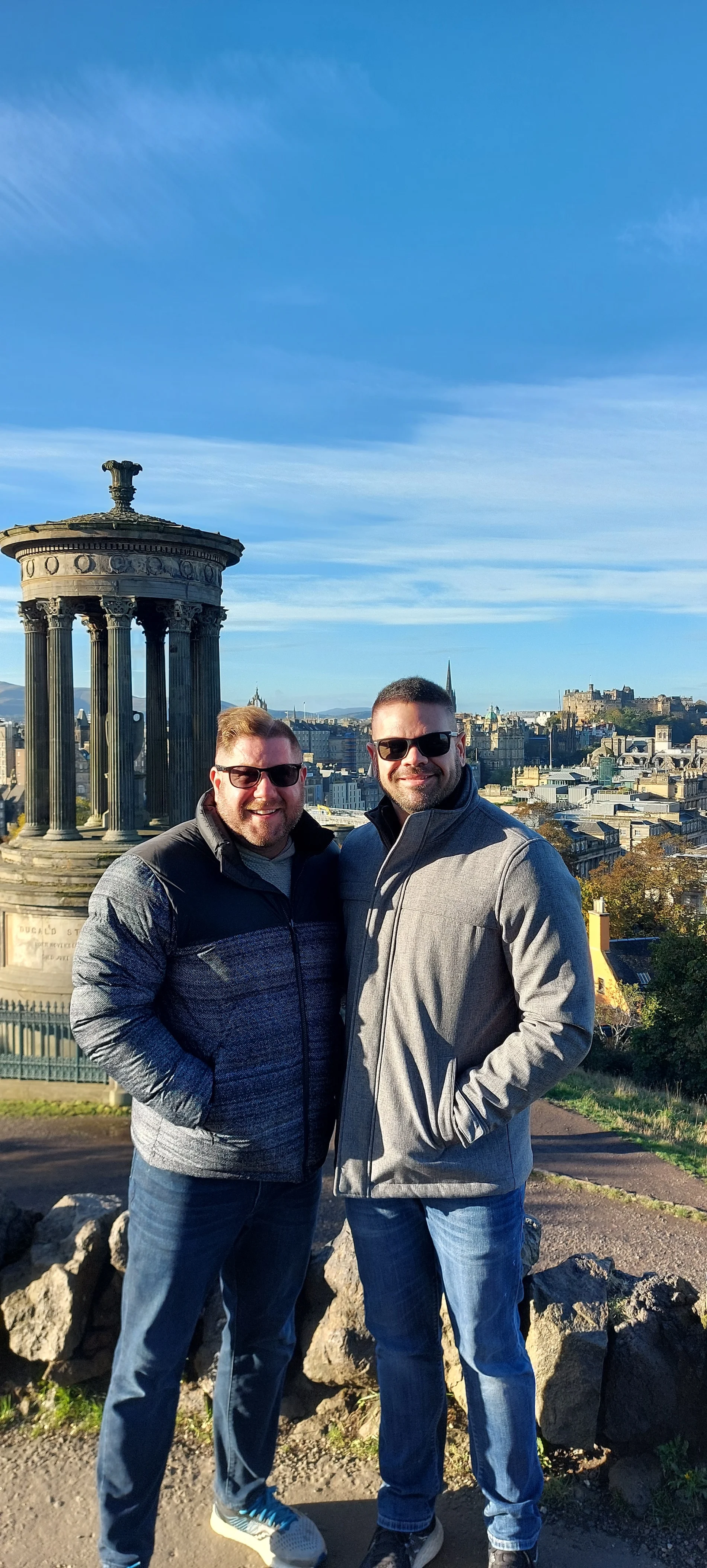 Two men posing at Calton Hill with Edinburgh cityscape behind them