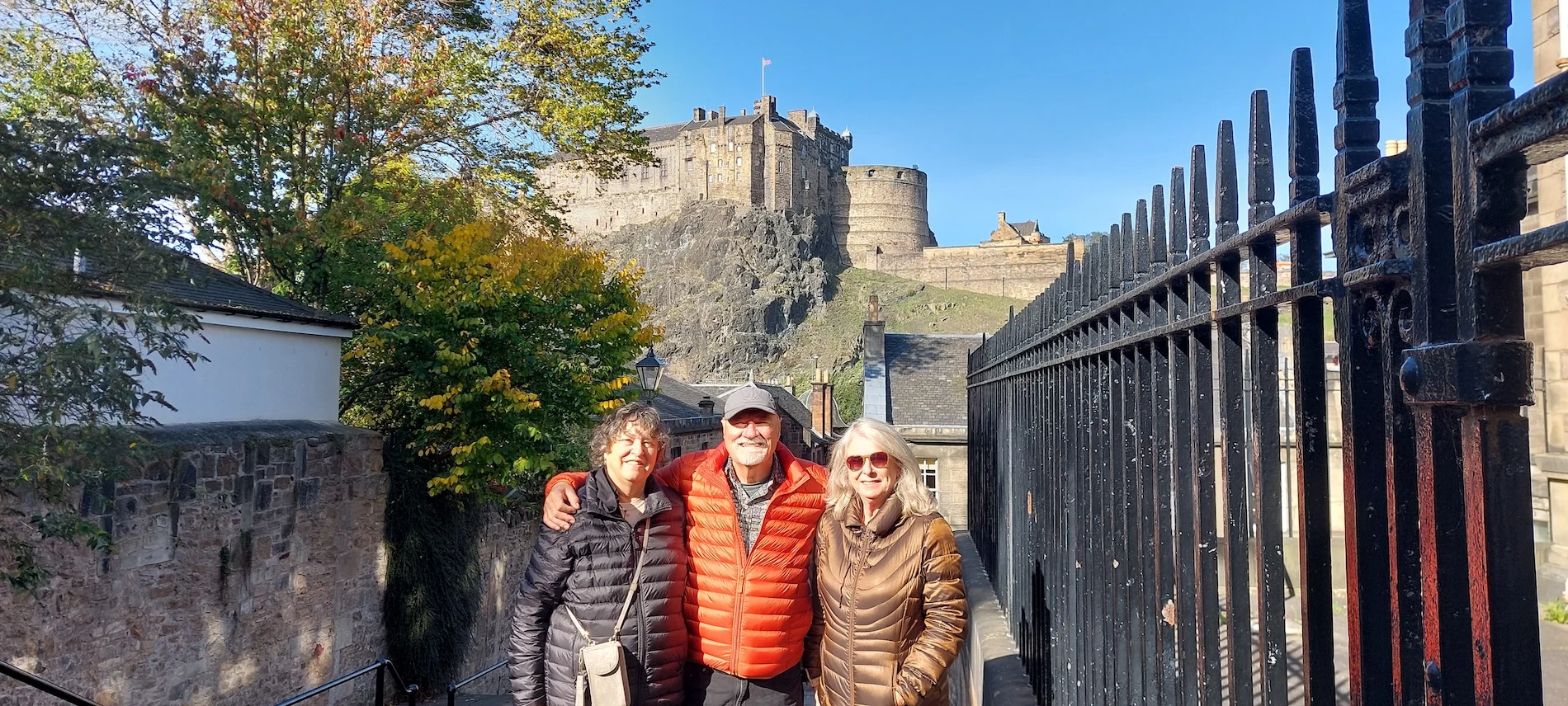 Three tourists posing in front of Edinburgh Castle on a sunny day