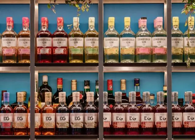Display of colorful Edinburgh gin bottles on blue shelves in distillery shop window.