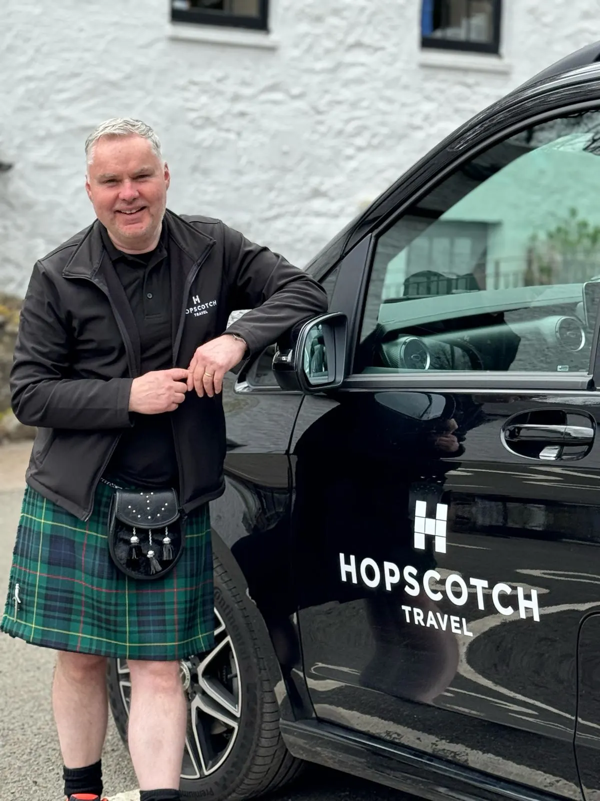 Scottish tour guide in kilt standing beside Hopscotch Travel vehicle