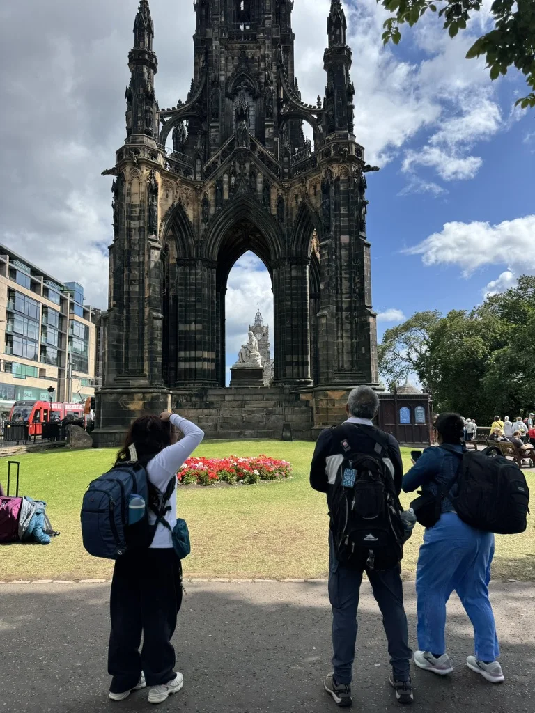 Tourists photographing the Scott Monument gothic stone arch in Edinburgh city center.