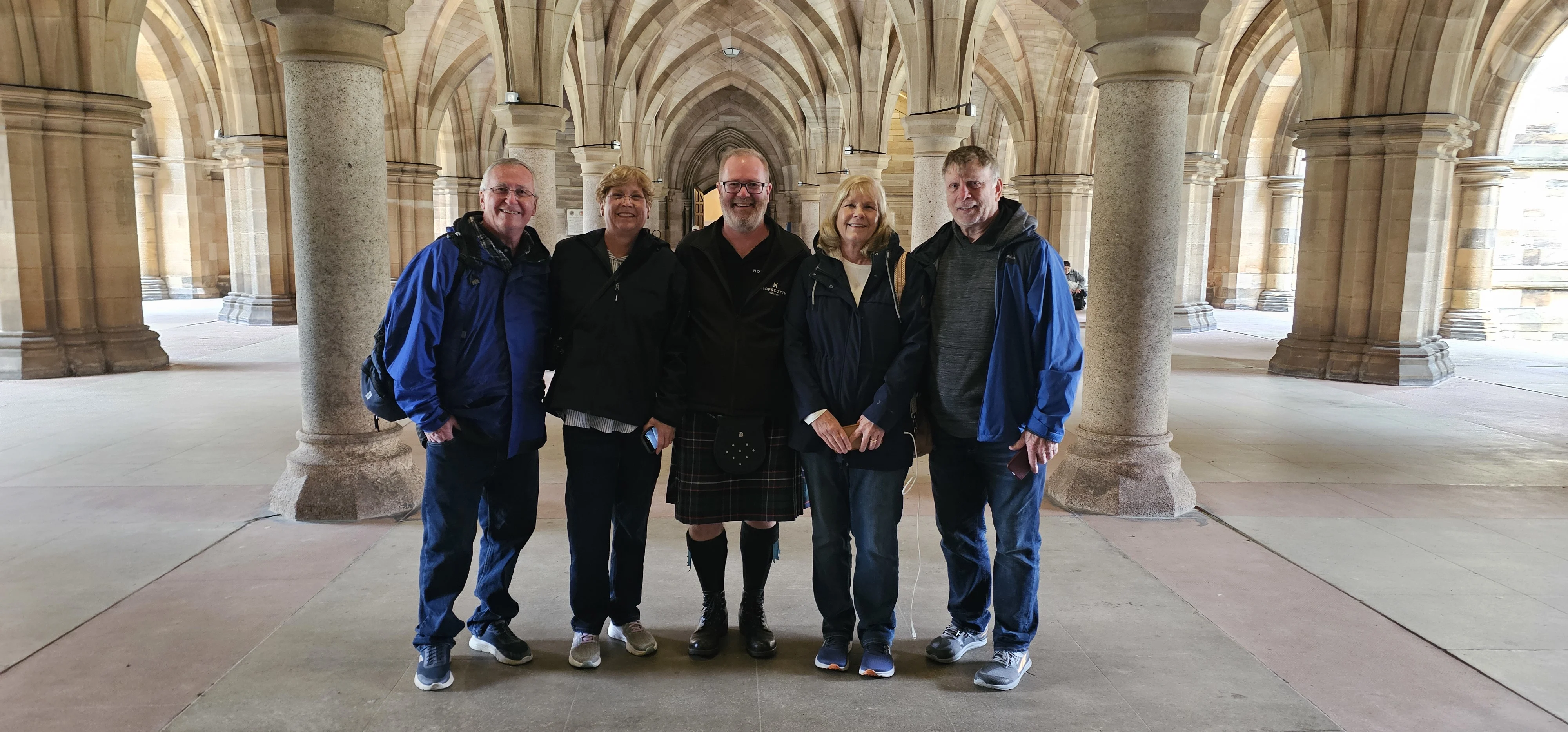 Group of five tourists posing in Gothic cathedral arches, Scotland.