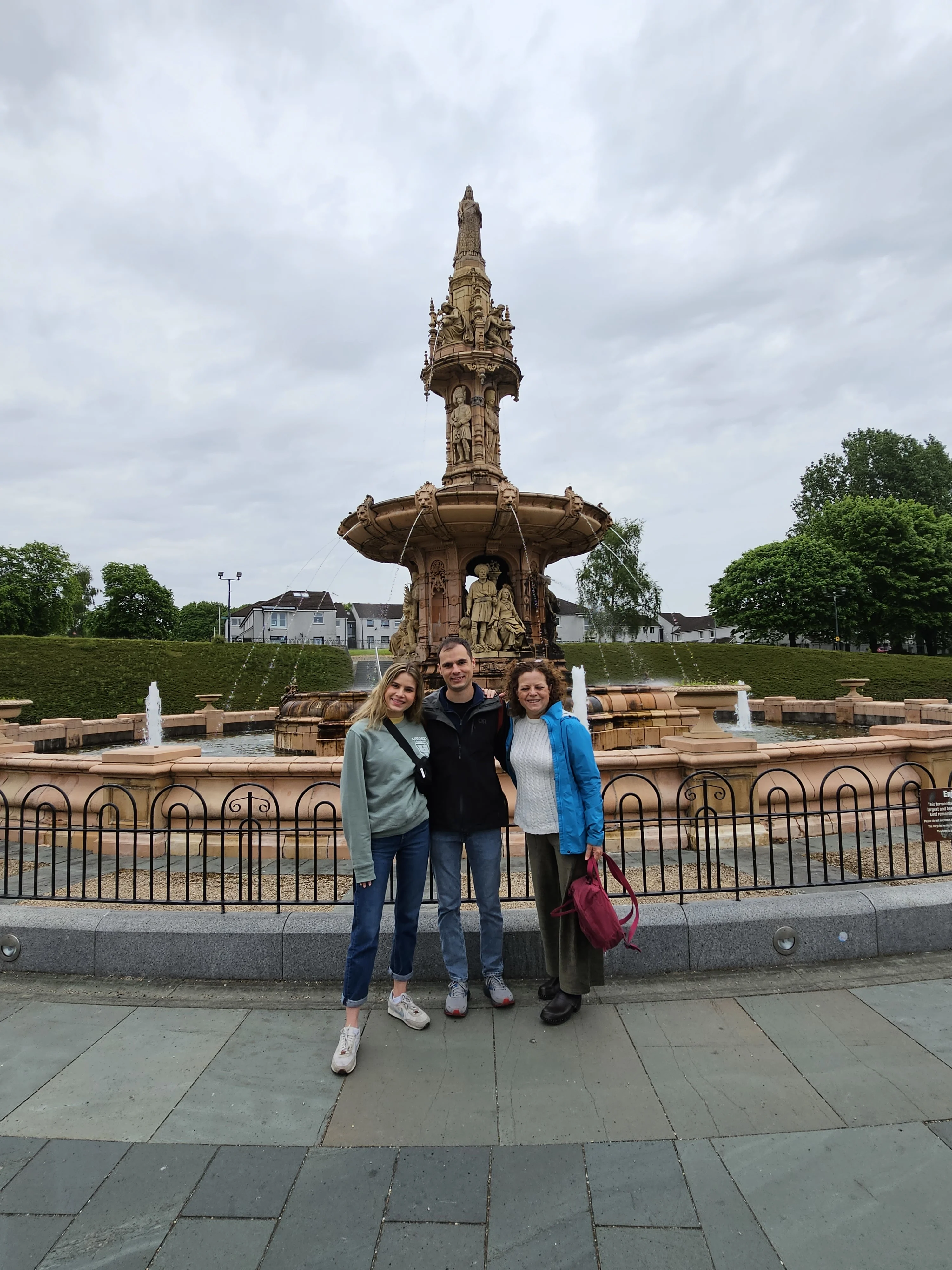 Three people posing at ornate stone fountain in Scottish town square