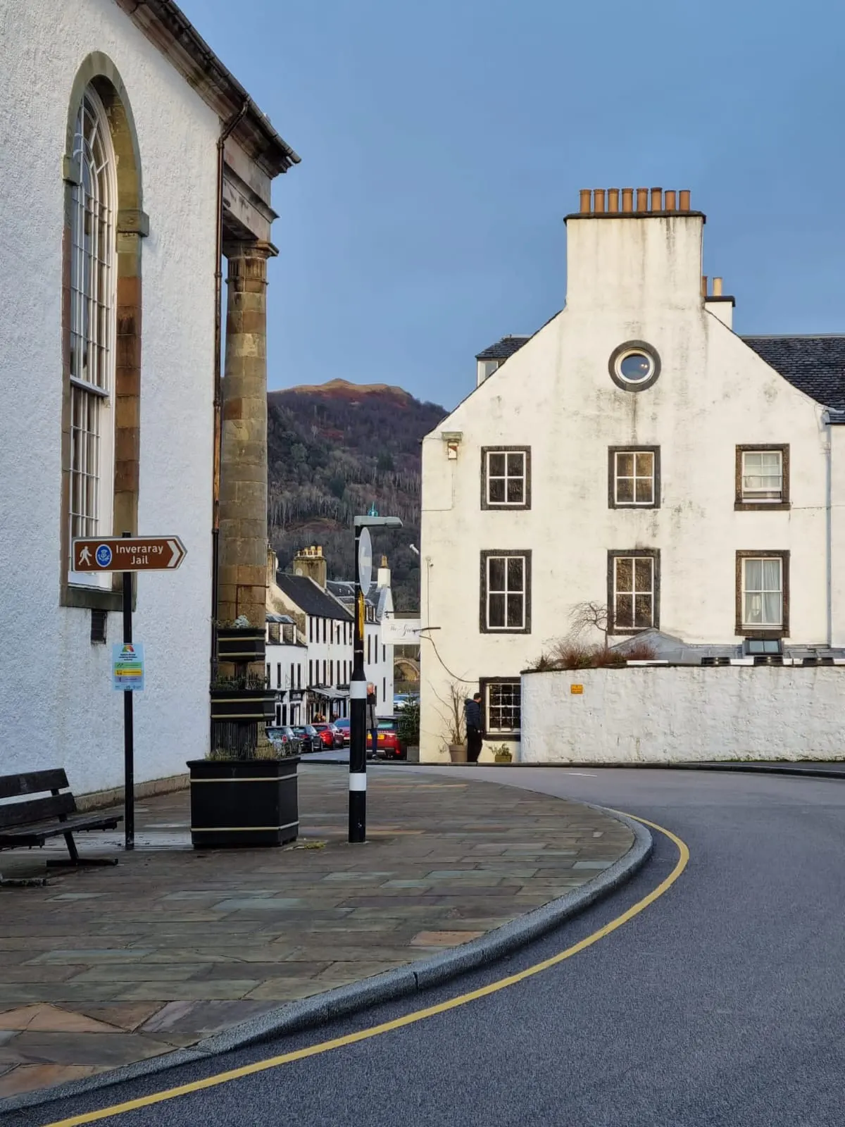White-washed Scottish village street with historic buildings and mountains beyond