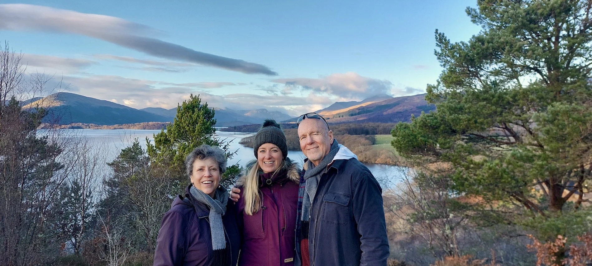 Three people smiling at scenic Scottish loch with mountains and trees