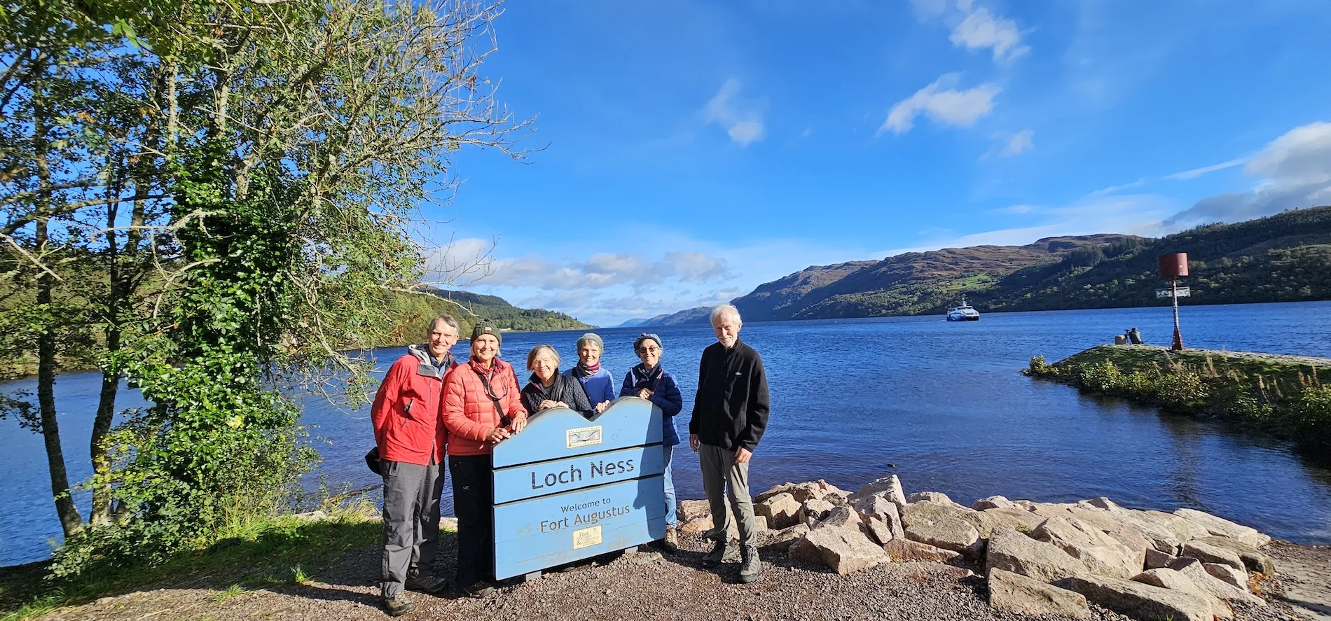 Group of tourists posing with Loch Ness sign at Fort Augustus Scotland