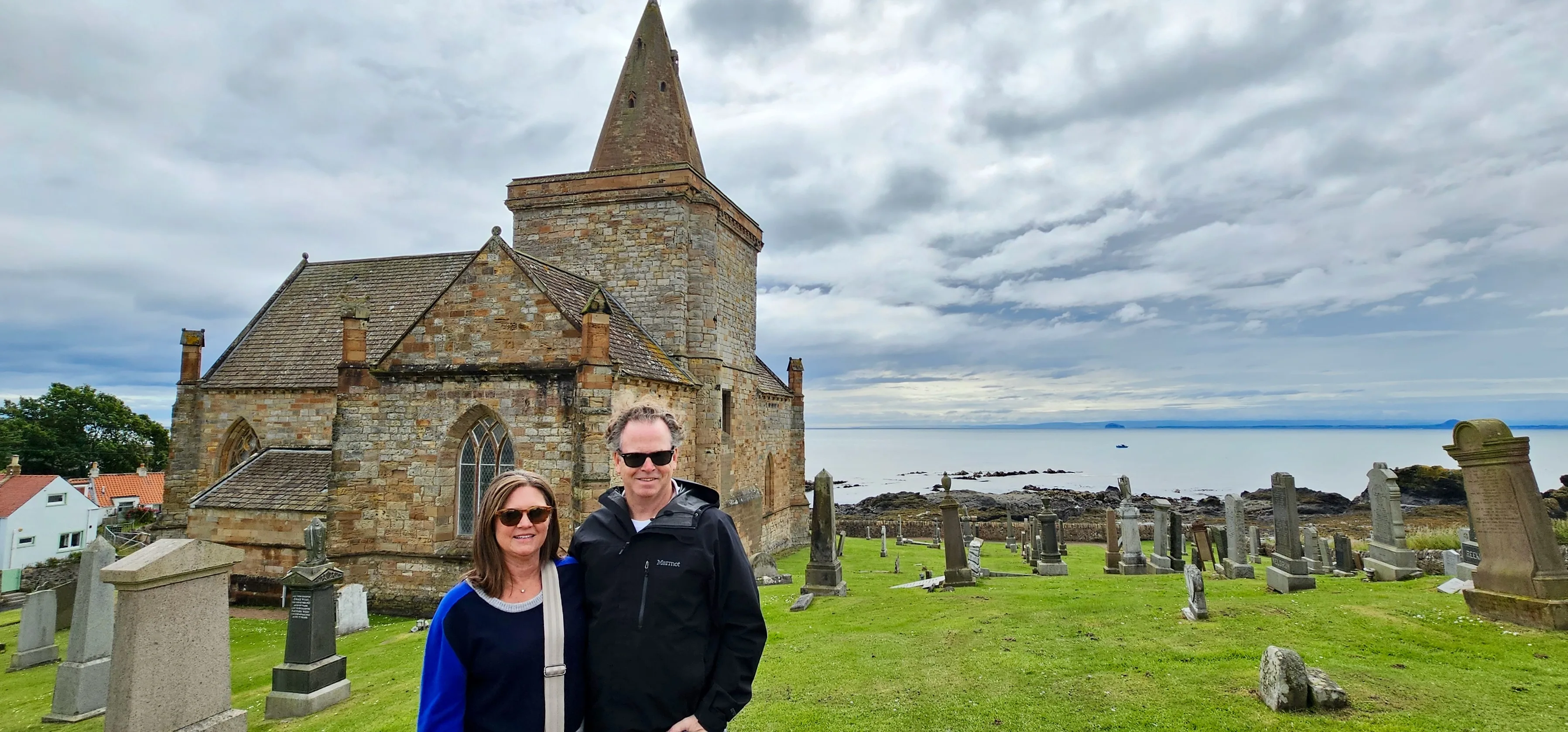 Couple posing at historic stone church with graveyard overlooking Scottish coastline