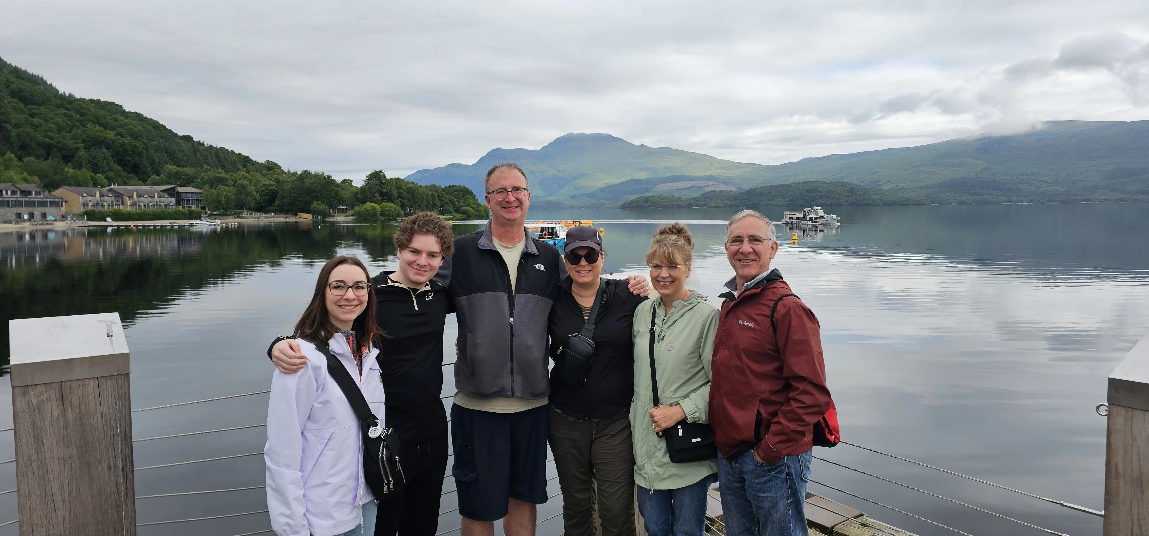 Group of six people posing on a Scottish loch pier with mountains behind them