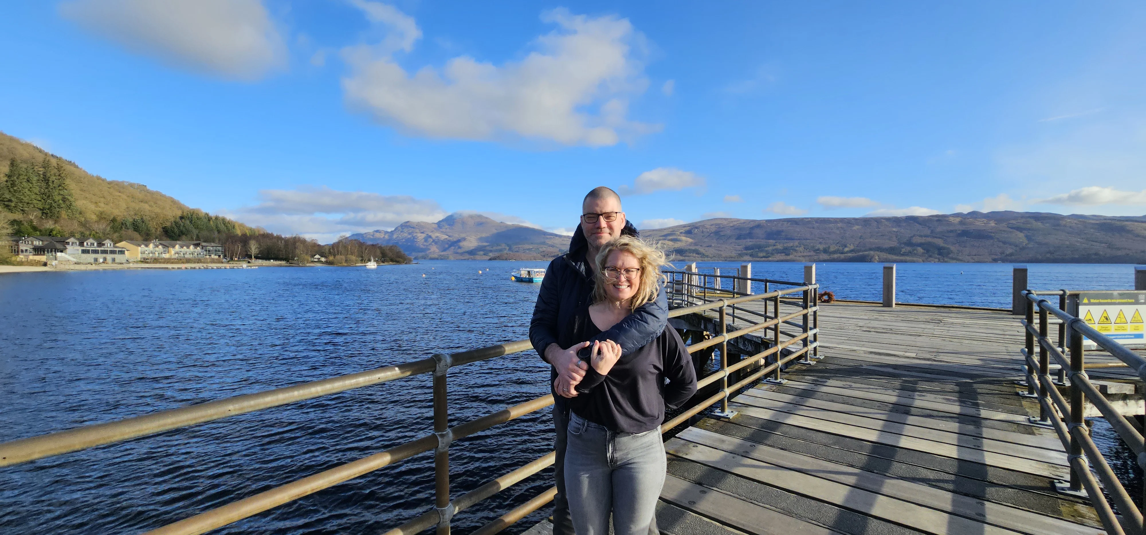 Couple posing on wooden pier overlooking Scottish loch and mountains
