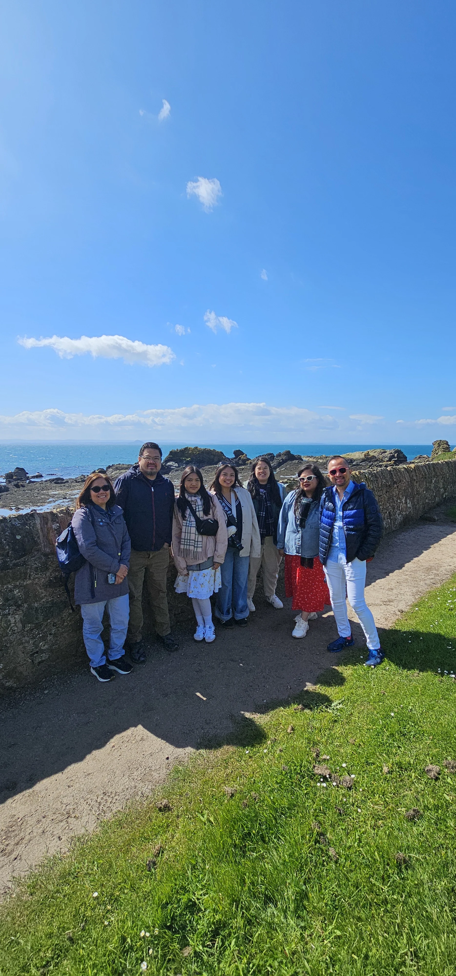 Group of tour participants posing on Scottish coastal cliffs by blue sea