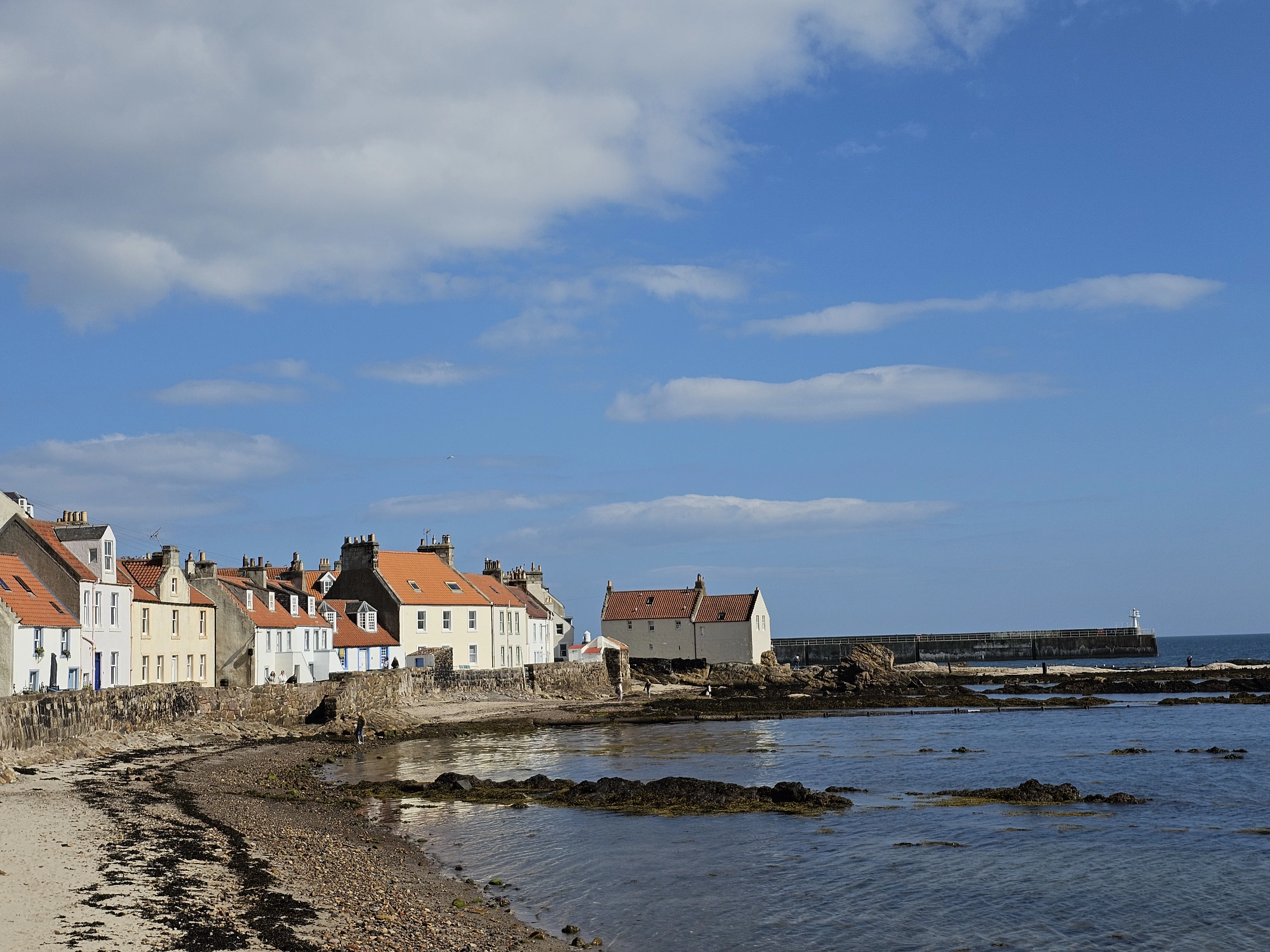 Colorful stone cottages line a Scottish coastal village beach with pier.