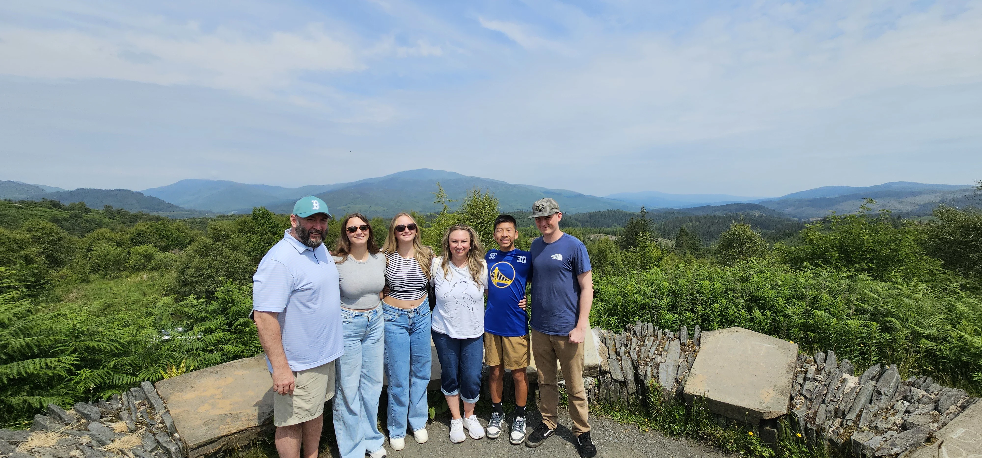 Group of six people posing at scenic Scottish mountain viewpoint overlook