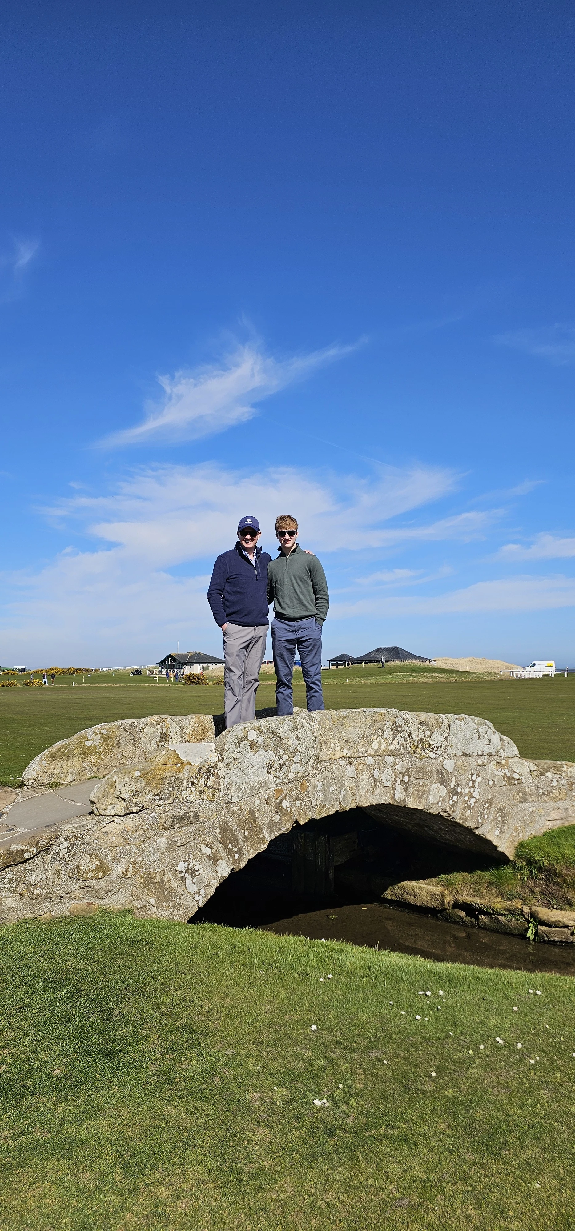 Two visitors standing on ancient stone bridge in Scottish countryside