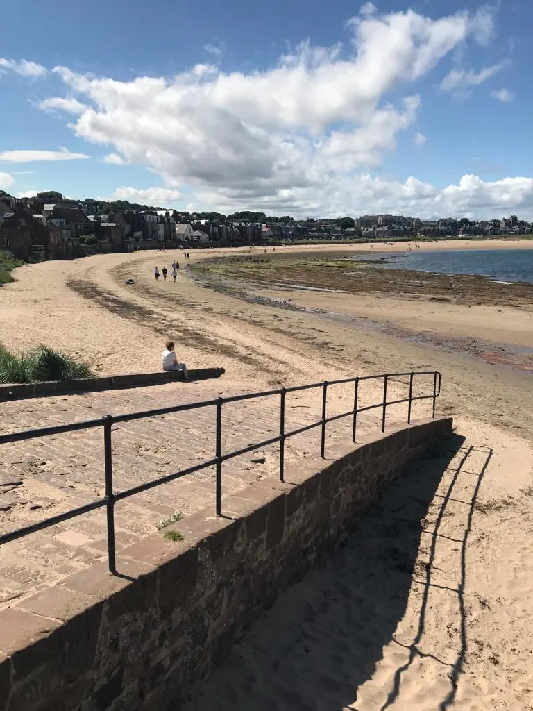 Scottish coastal beach town with sandy shore and seaside buildings on hillside