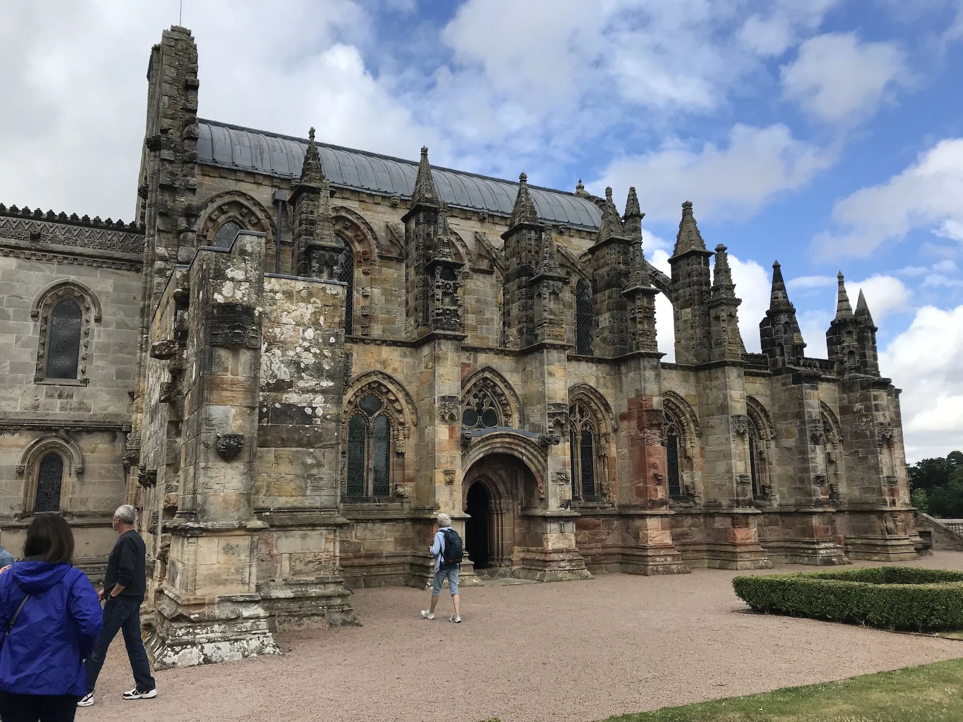 Historic stone chapel with Gothic architecture and visitors on courtyard grounds