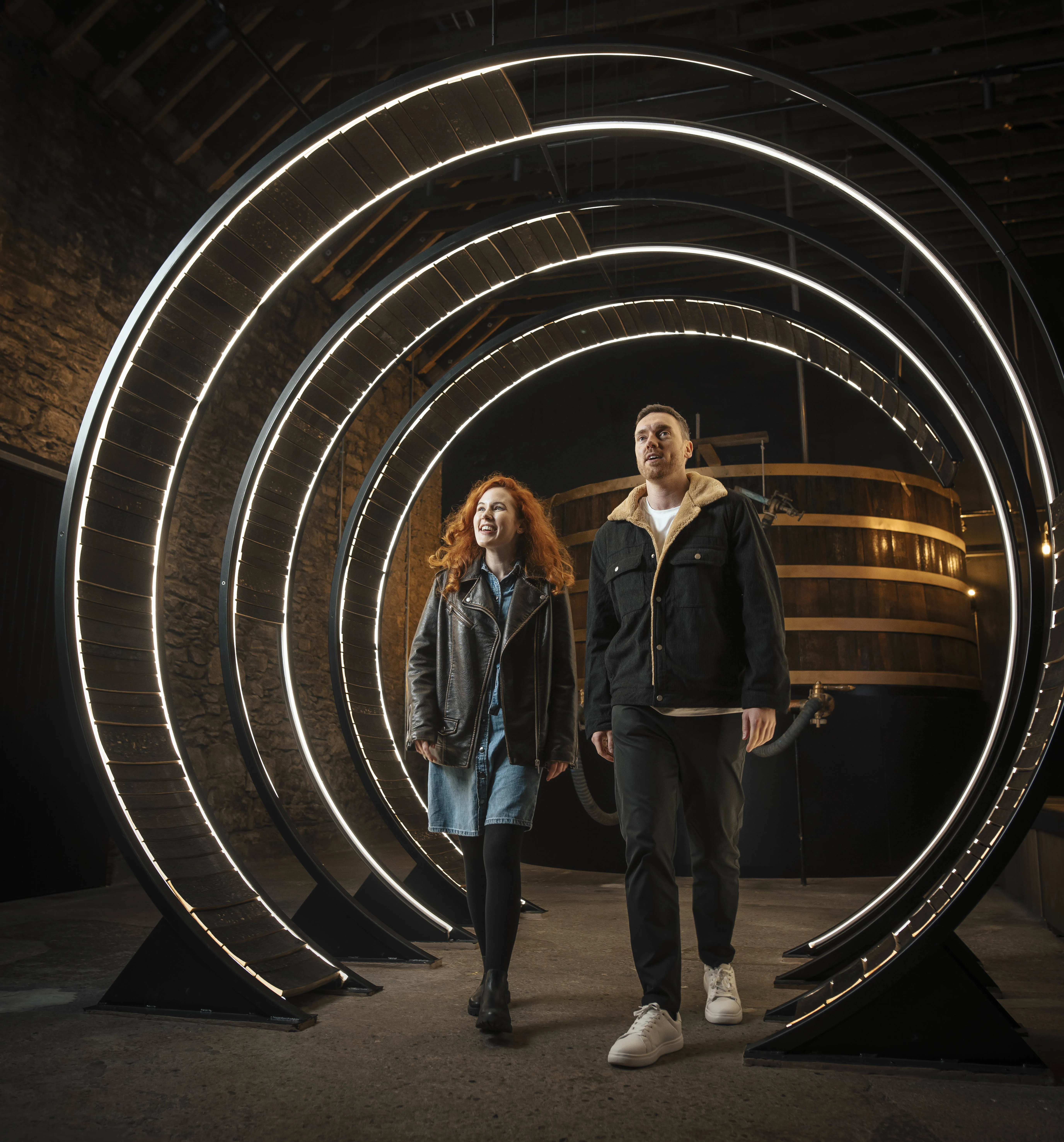 Two visitors admire glowing circular installation at Scottish whisky distillery