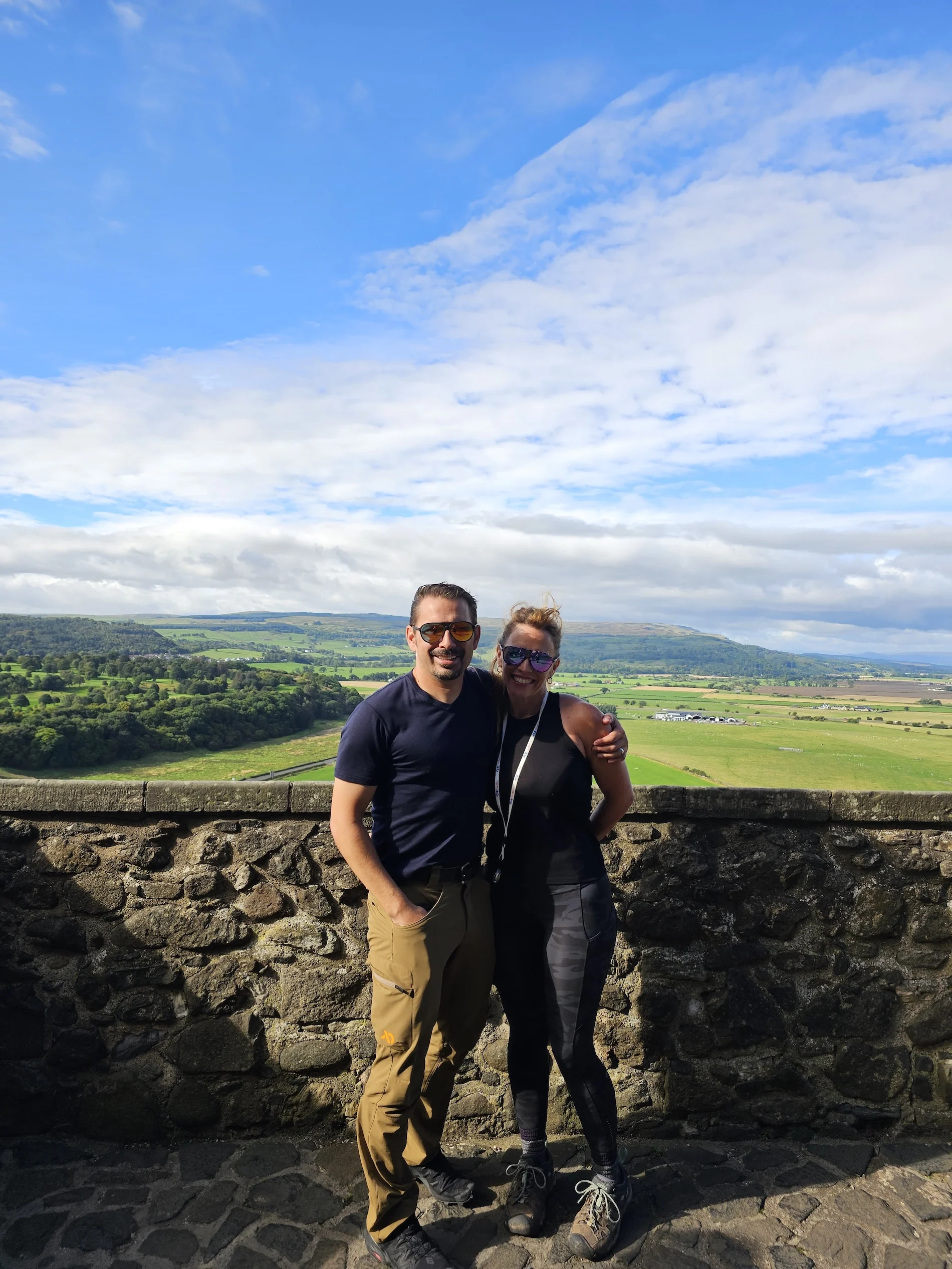 Couple posing at stone viewpoint overlooking rolling Scottish countryside and valleys