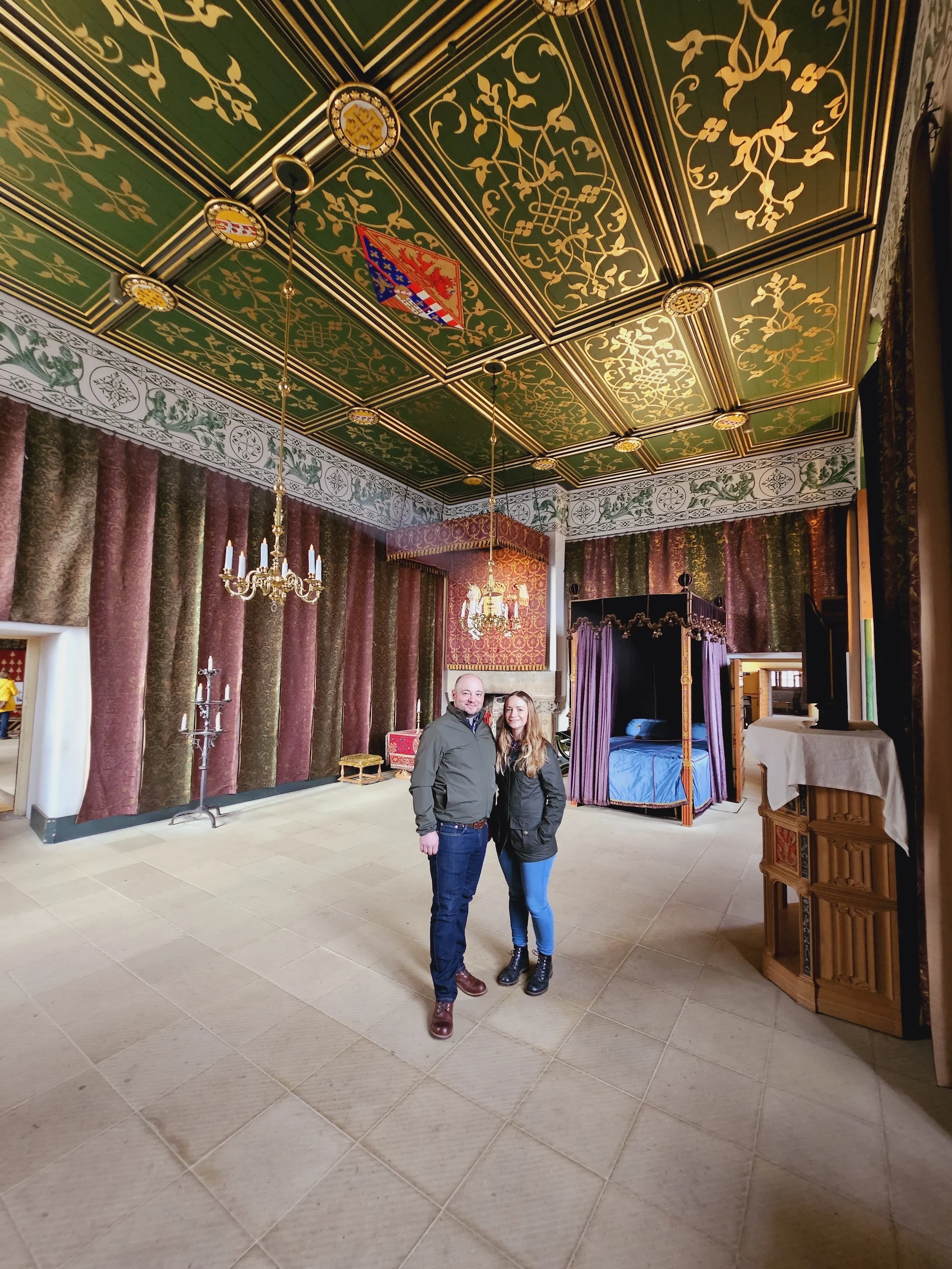 Couple posing in ornate Scottish castle bedroom with gilded ceiling and four-poster bed