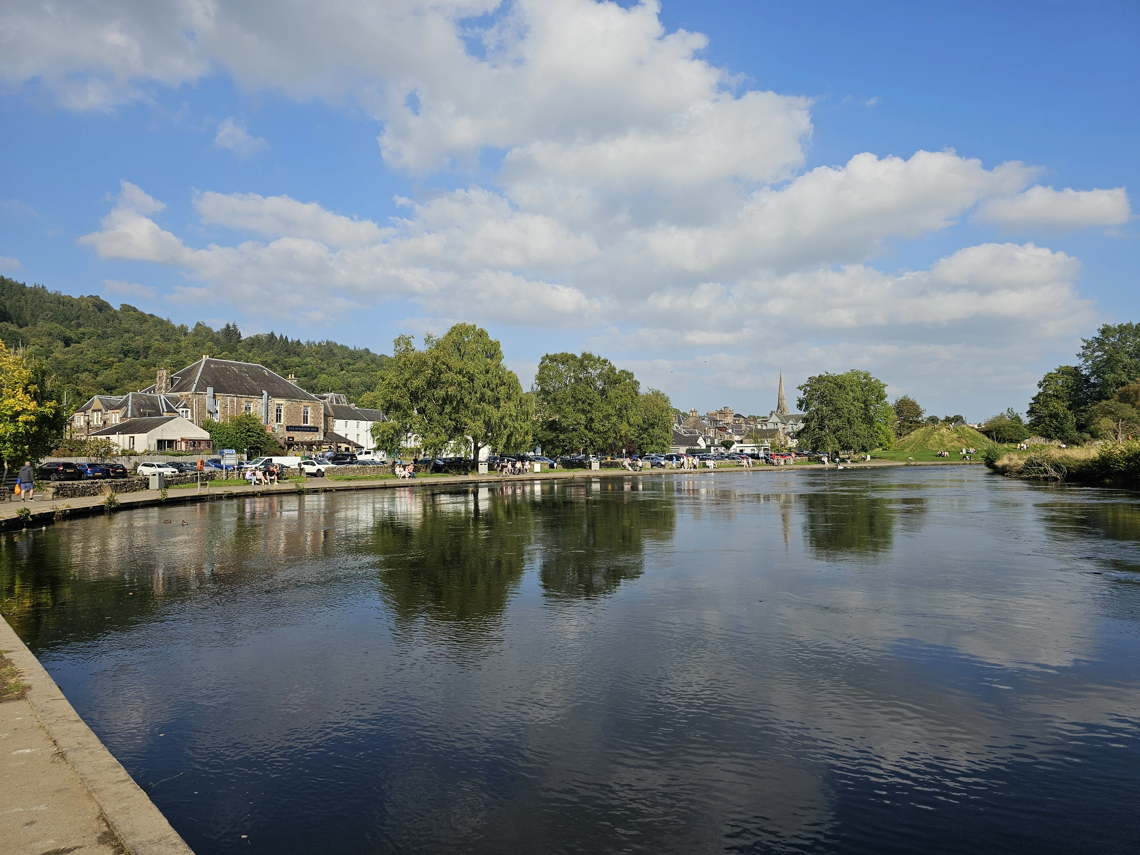 Scottish riverside village with stone buildings and church spire reflected in calm water