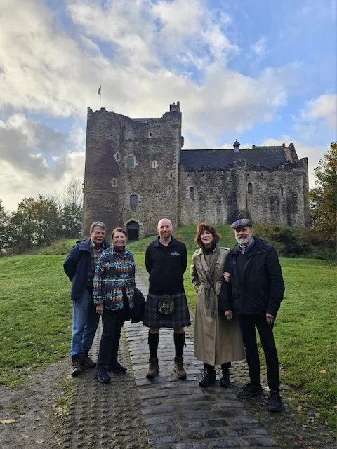 Group of five people standing in front of historic Scottish castle ruins.