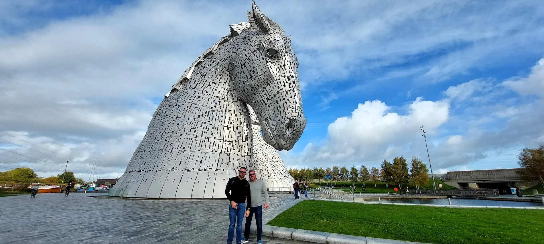 Two visitors posing in front of the Kelpies horse sculpture in Scotland