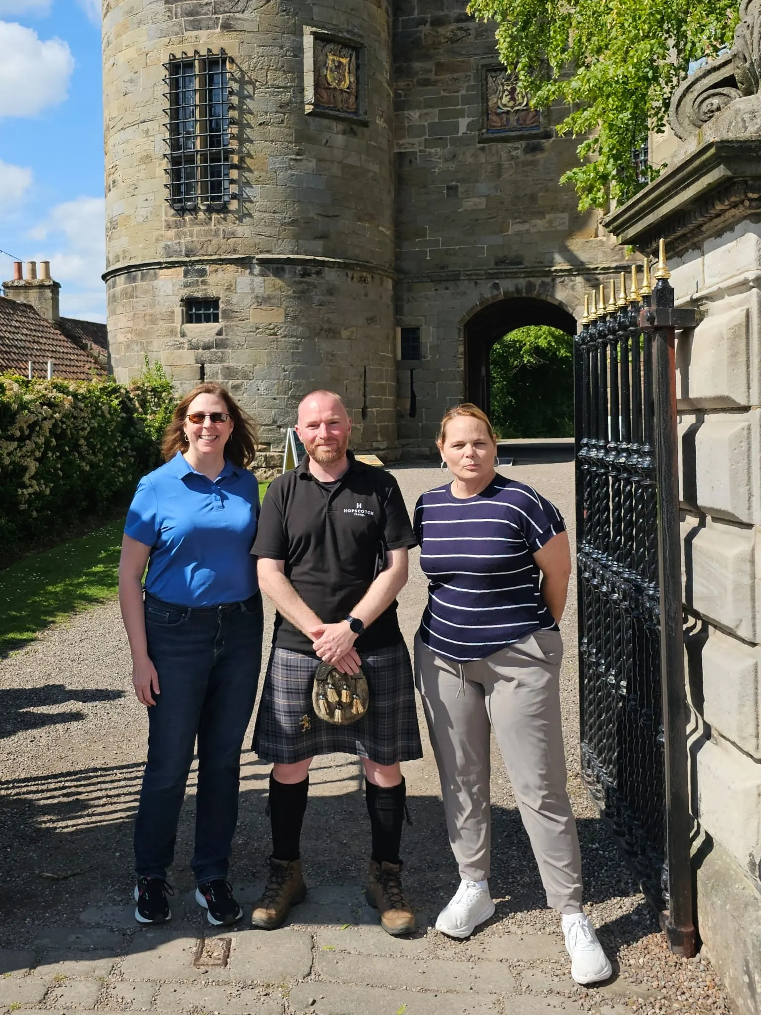 Three people posing in front of historic Scottish castle tower.