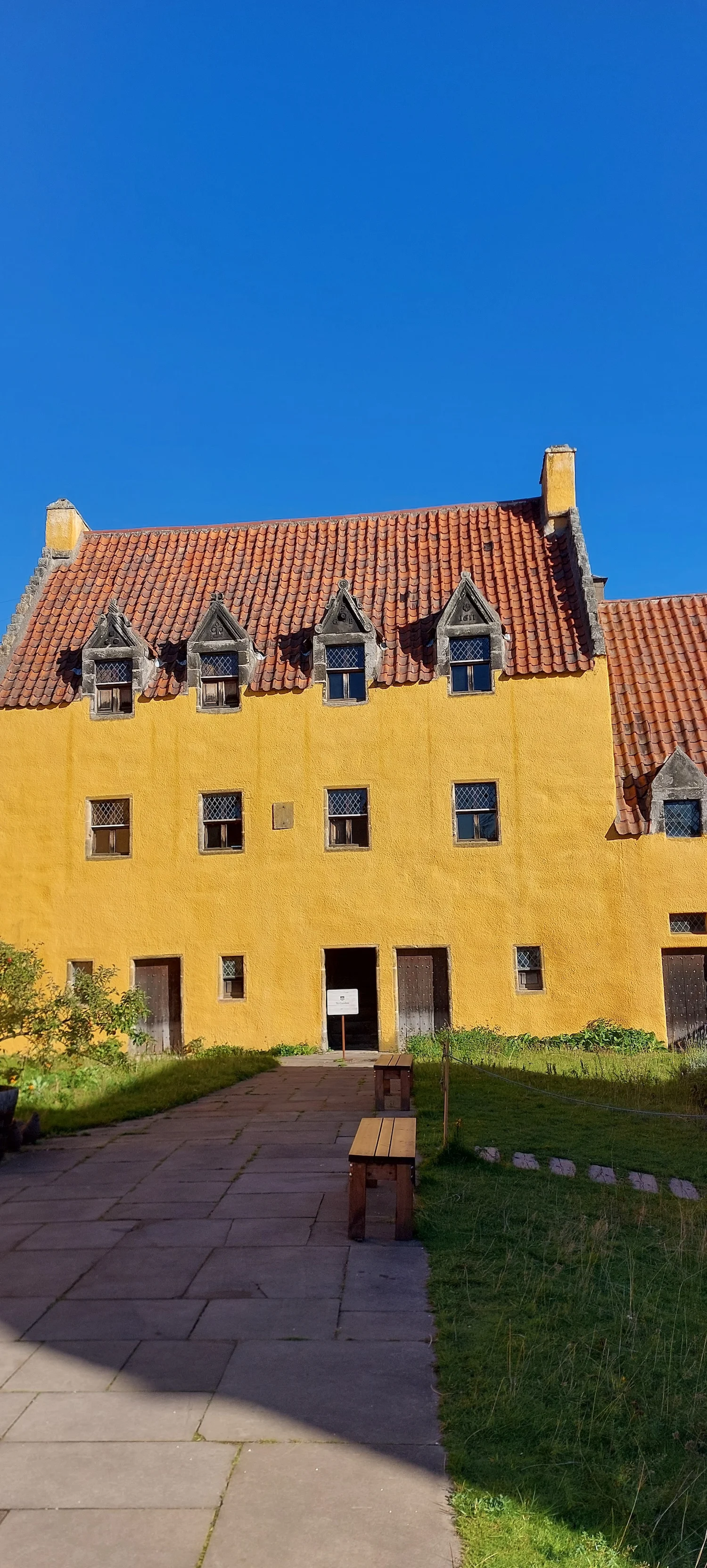 Bright yellow Scottish historic building with red tile roof and dormer windows