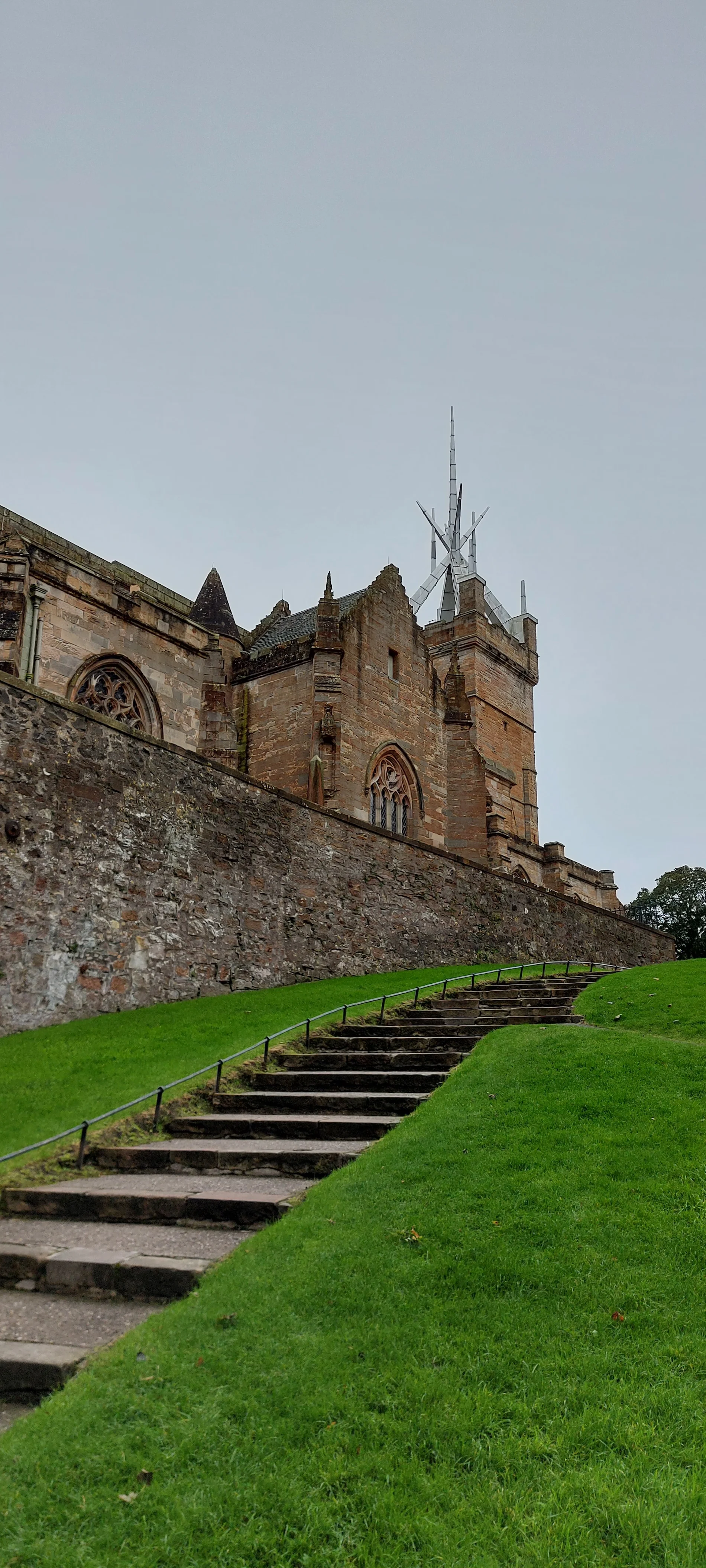 Stone castle with tower and steps leading up green hillside