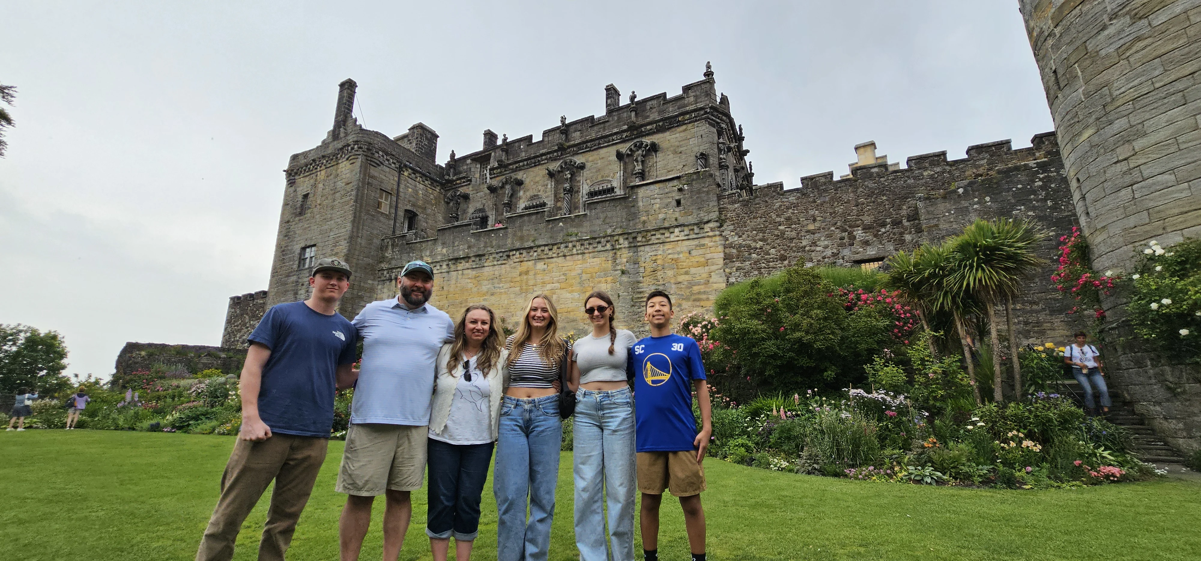 Group of six tourists posing in front of historic Scottish castle
