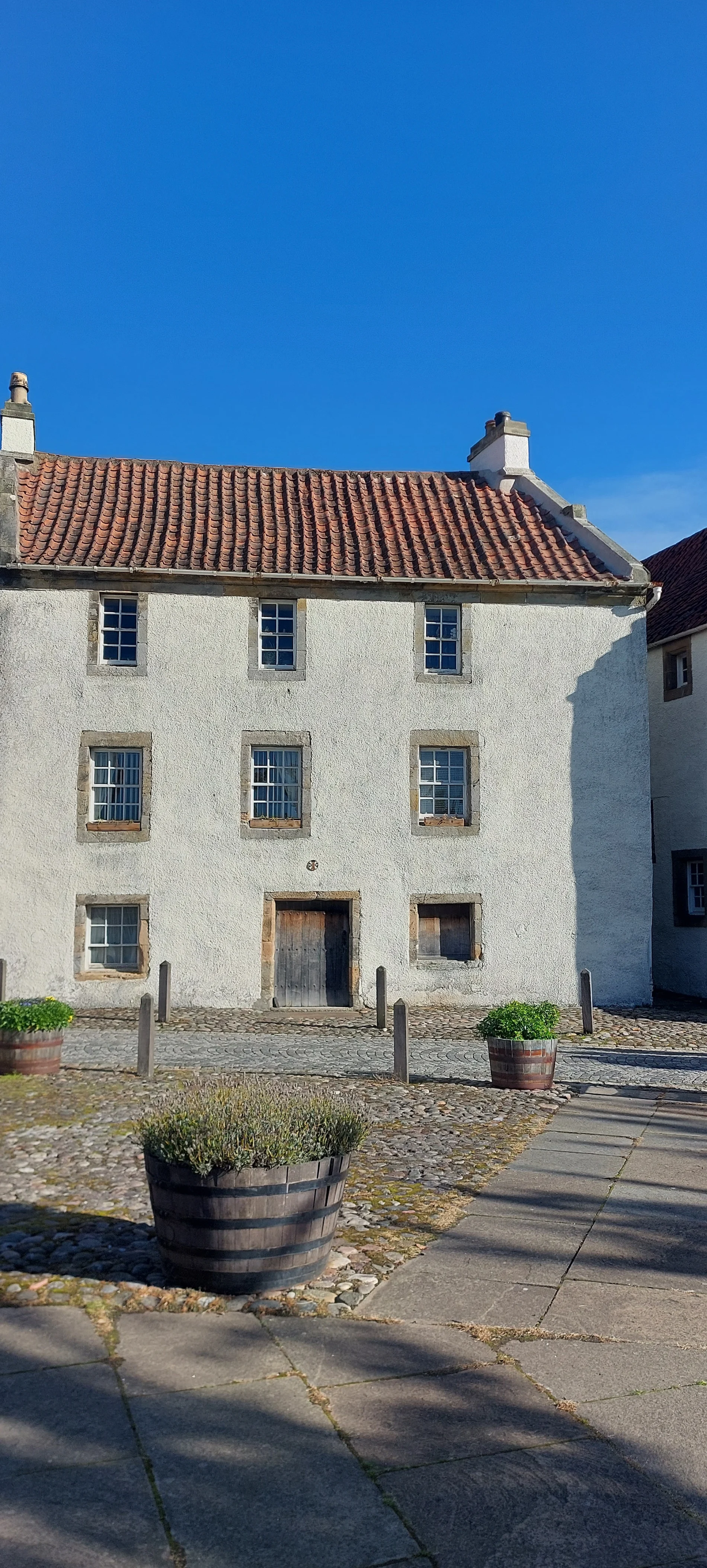 Traditional white stone Scottish cottage with terracotta roof and blue sky