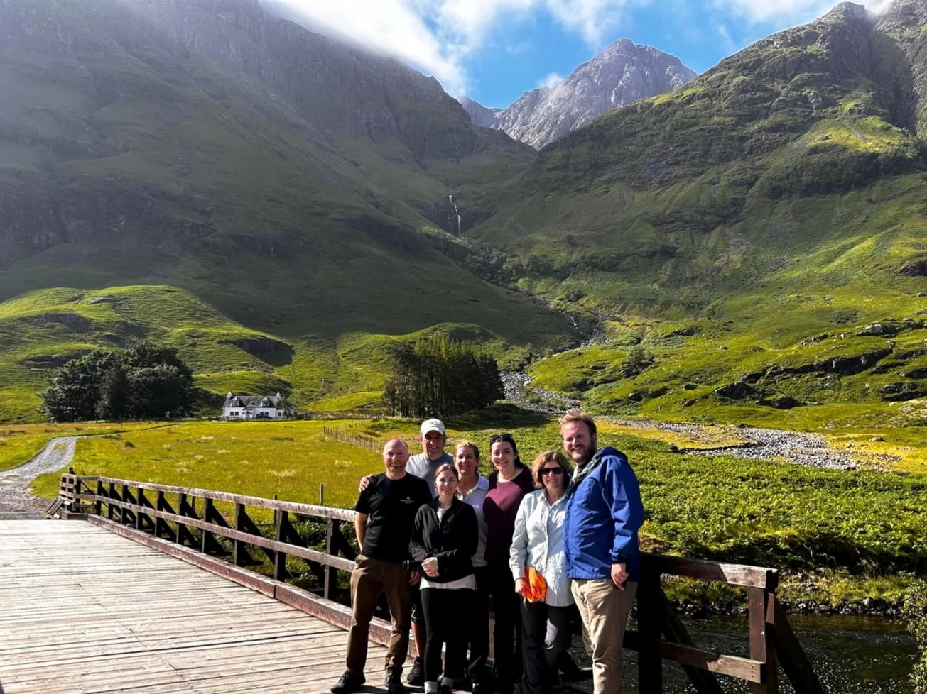 Tour group posing on wooden bridge in Scottish Highland valley with mountains