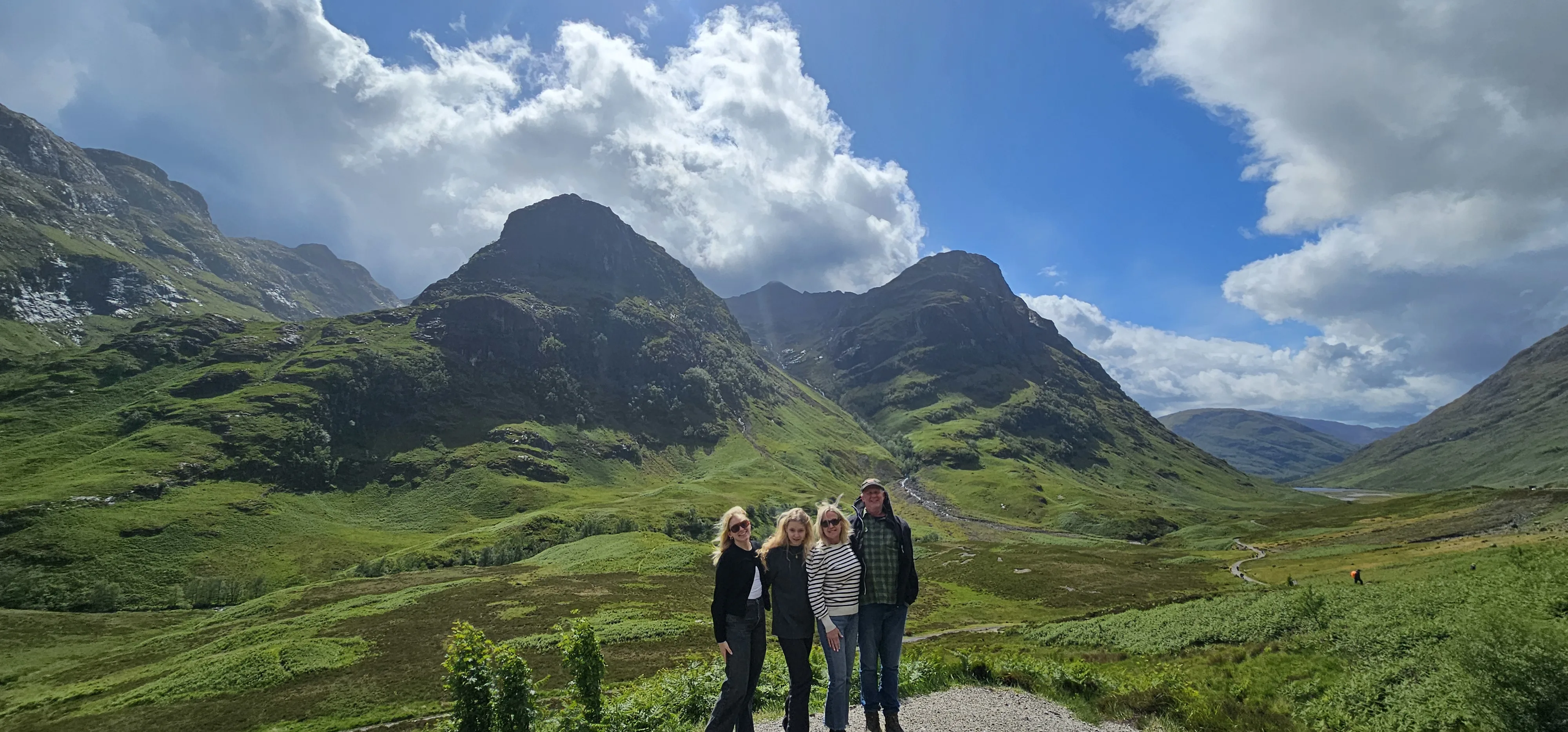 Four tourists posing in scenic Scottish Highland valley with mountains