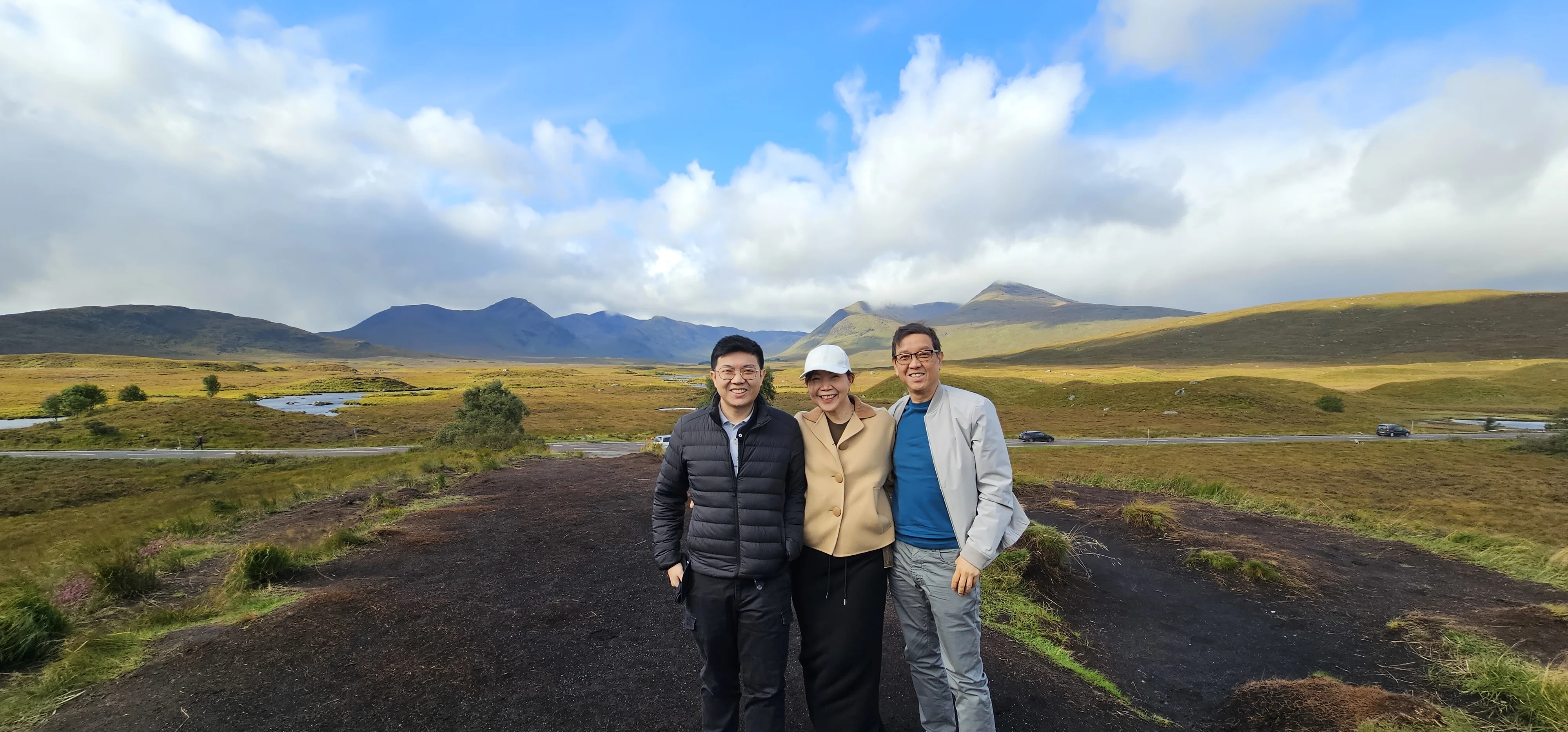 Three tourists posing in Scottish Highlands with mountains and moorland behind them