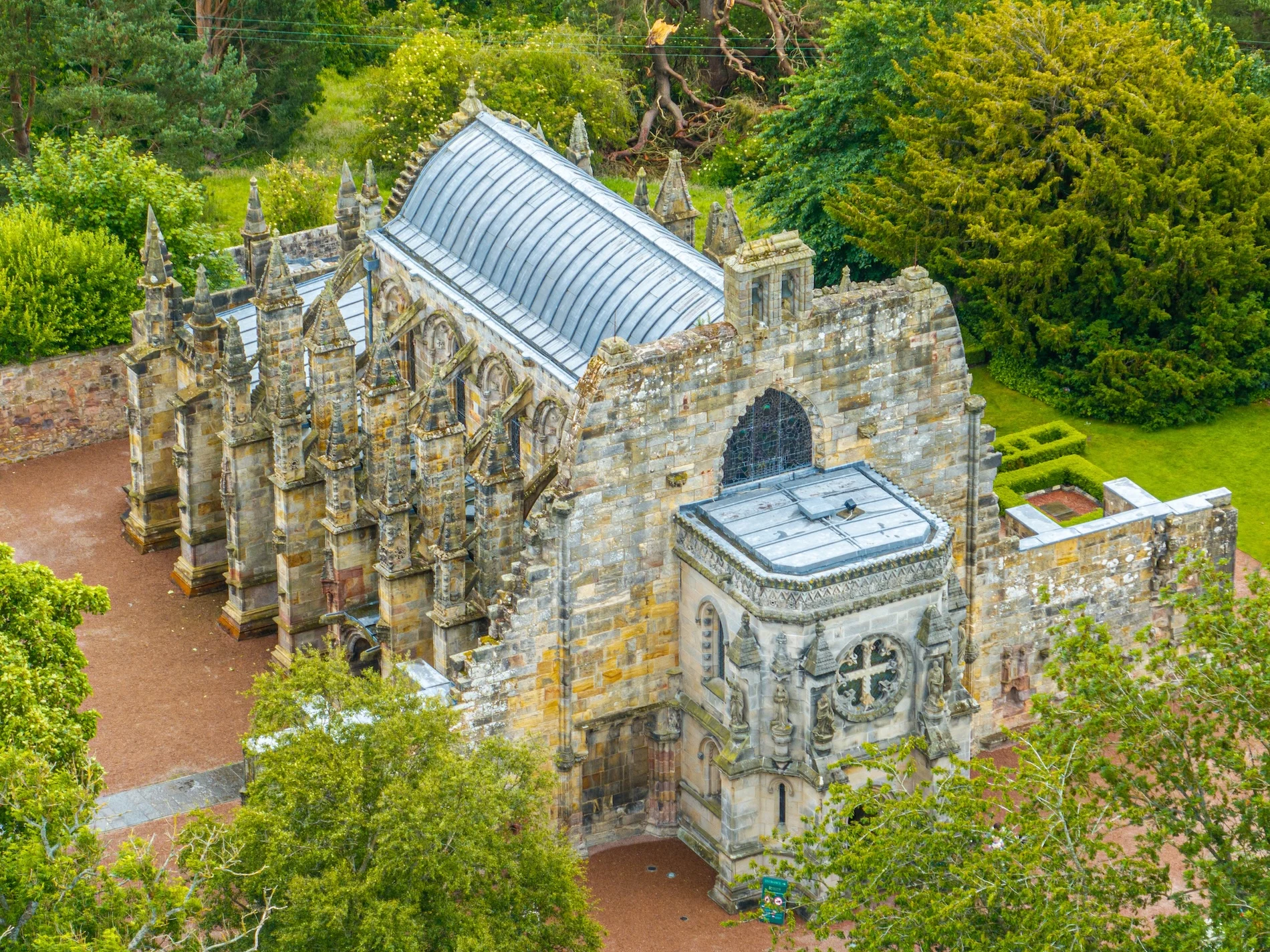 Aerial view of ornate Scottish stone chapel surrounded by green woodland trees