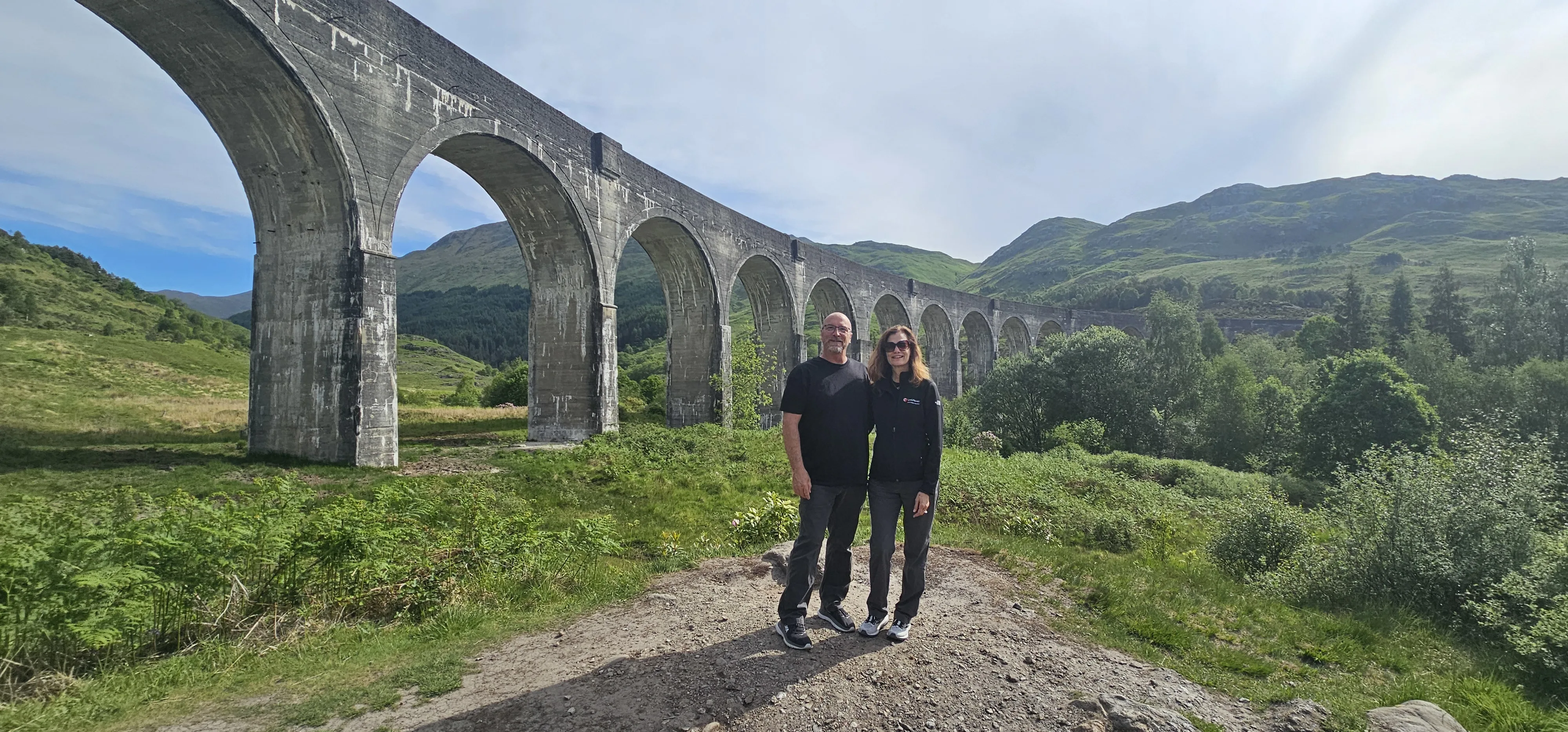 Couple posing at historic stone viaduct in Scottish Highlands landscape