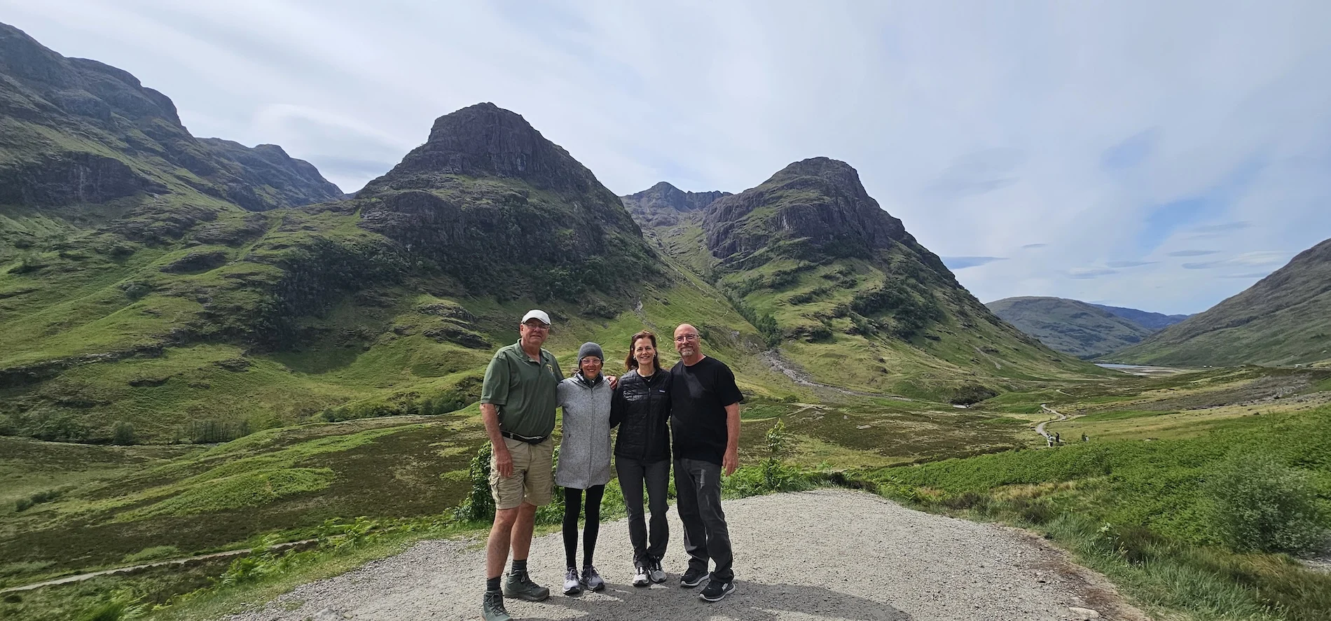 Four tourists posing in Scottish Highlands with dramatic mountain peaks behind them.