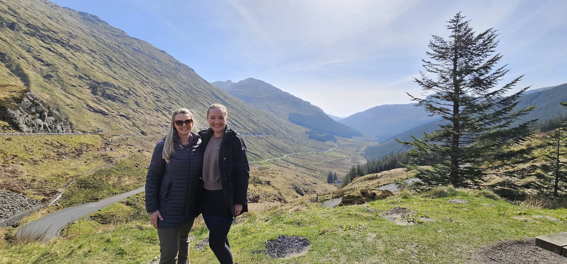 Two women posing in a Scottish Highland valley with mountains and trees