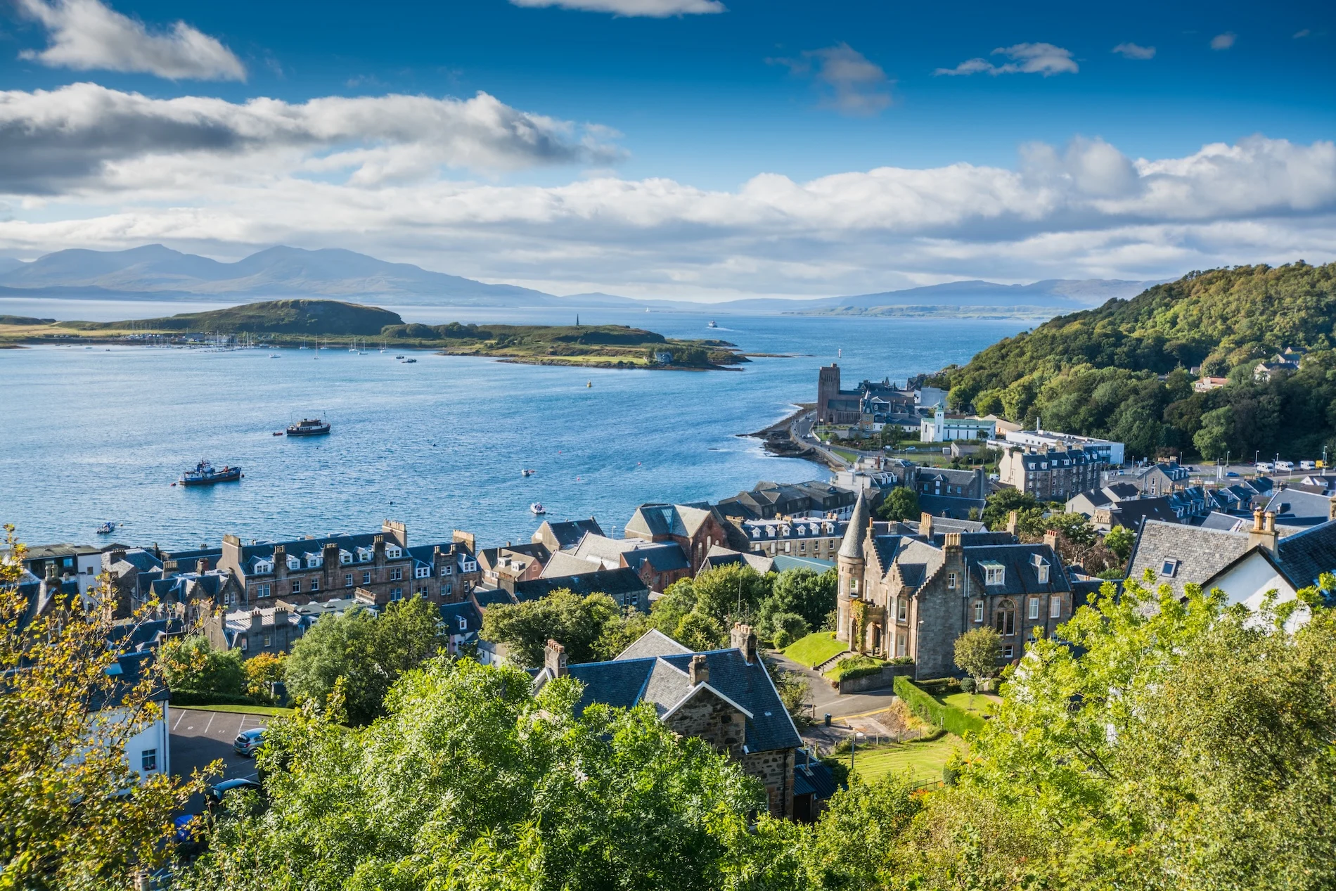 Coastal Scottish town overlooking blue sea with mountains and islands in distance