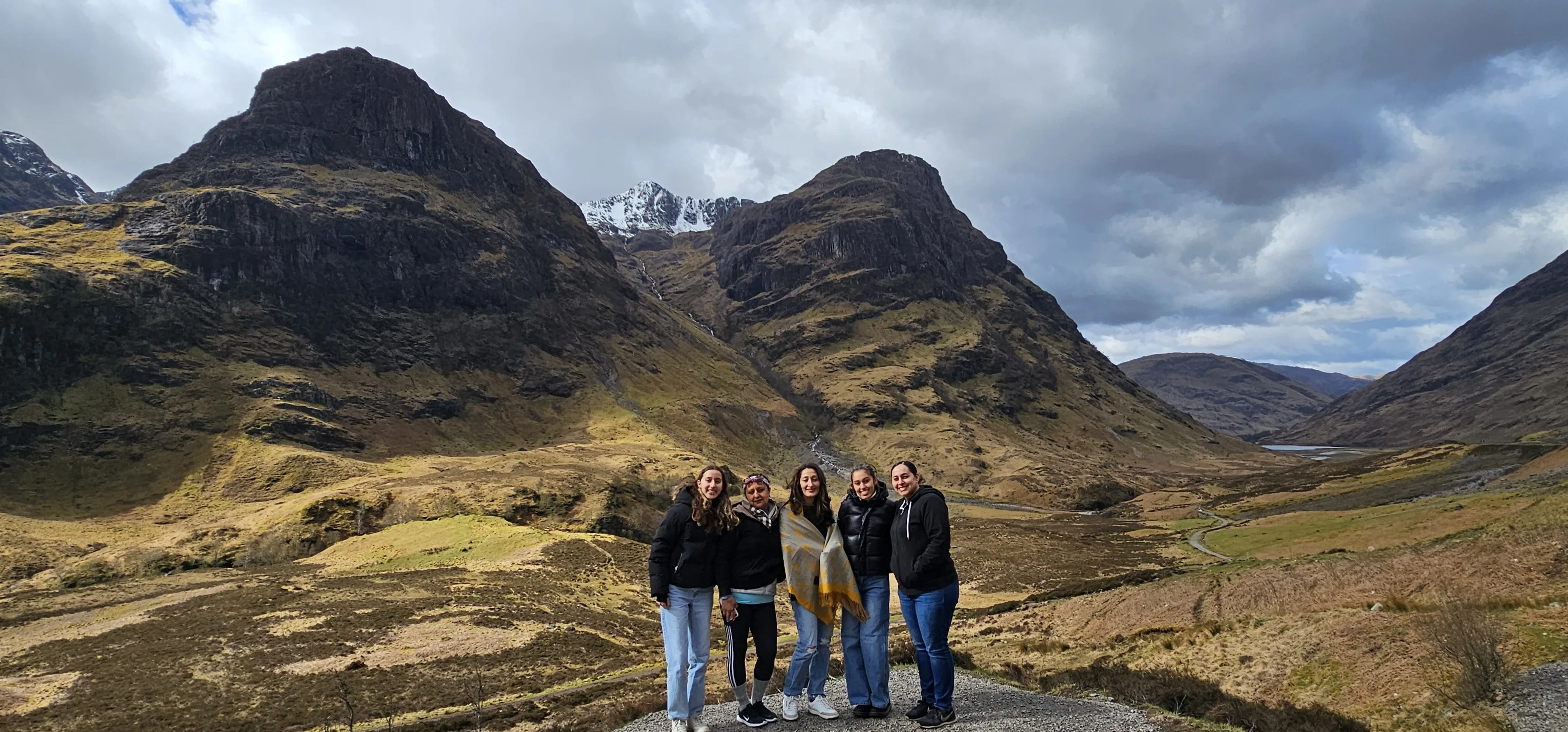 Group of five people posing in Scottish Highland valley with dramatic mountains behind