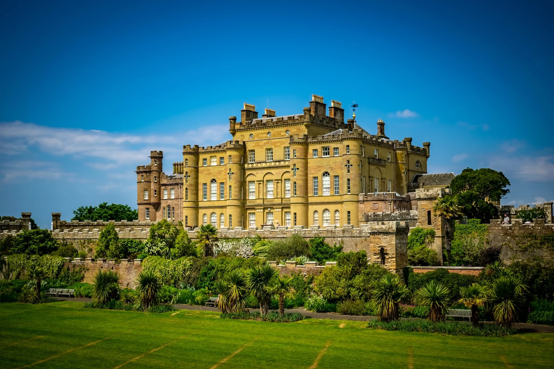 Historic yellow Scottish castle with manicured grounds and surrounding stone walls.