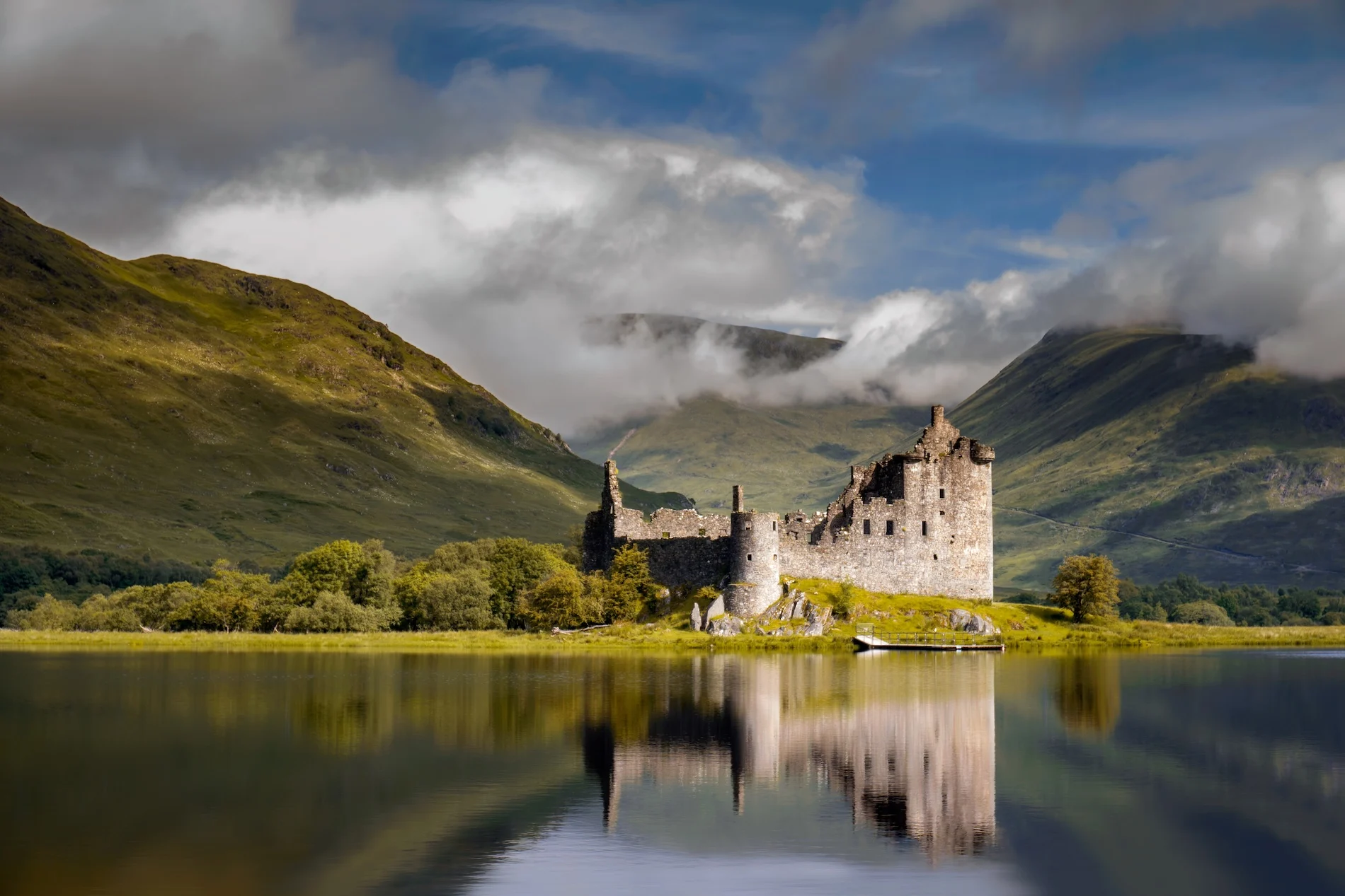 Kilchurn Castle reflected in calm loch with Scottish mountains and clouds behind