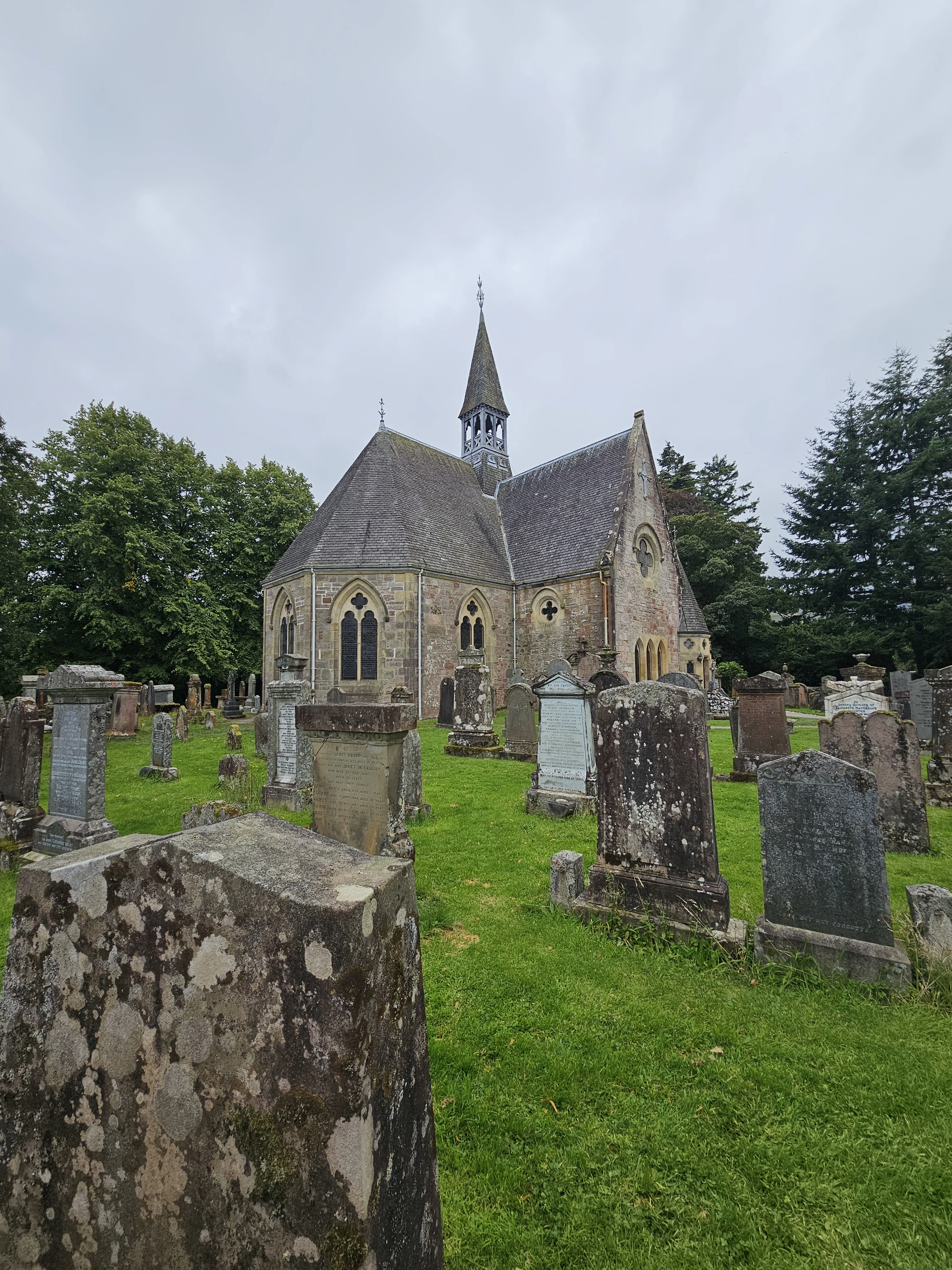 Historic Scottish stone church with graveyard surrounded by ancient headstones and trees.