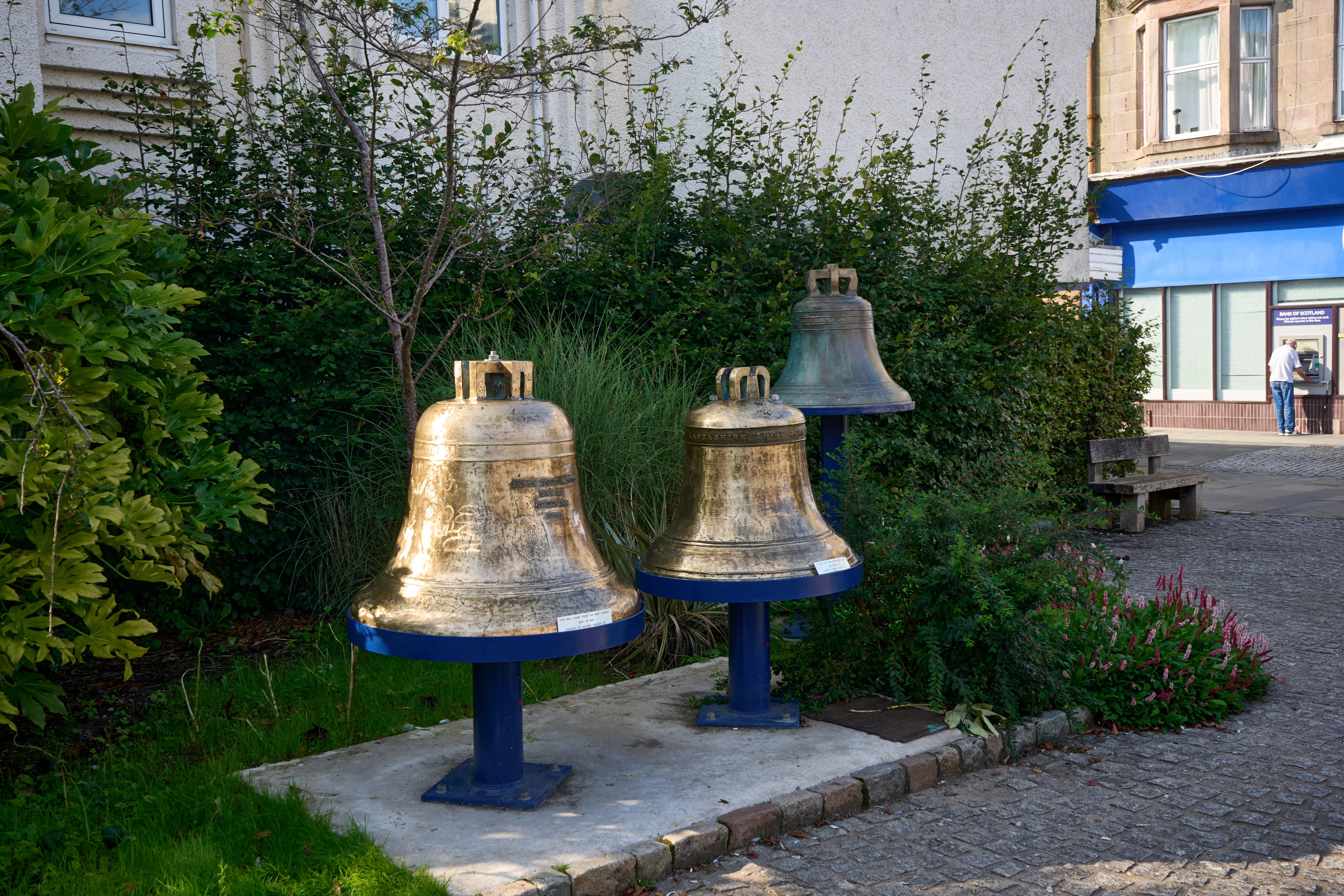 Three large bronze bells displayed on blue pedestals in Scottish town square
