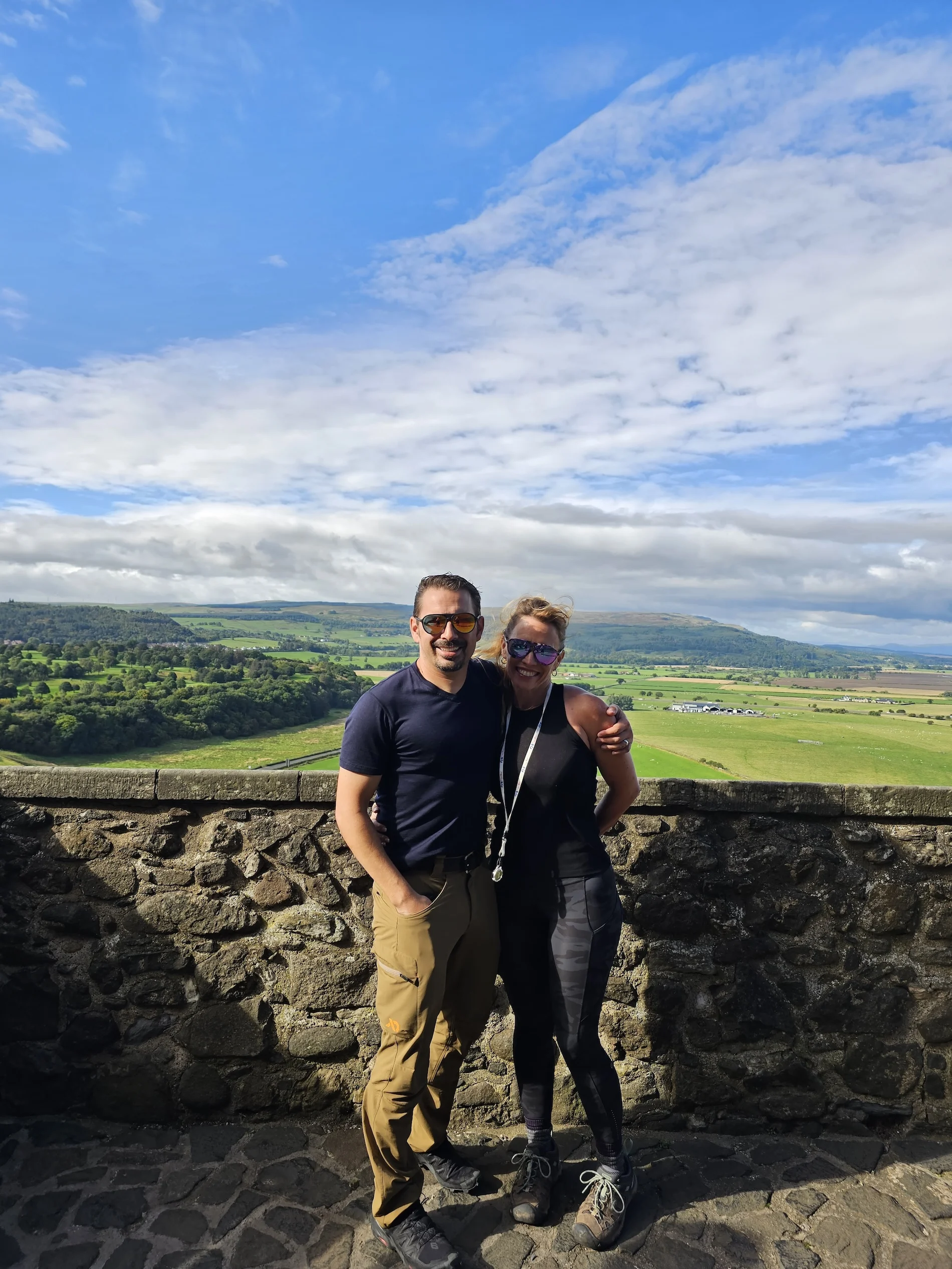 Couple posing at stone viewpoint overlooking Scottish valley landscape