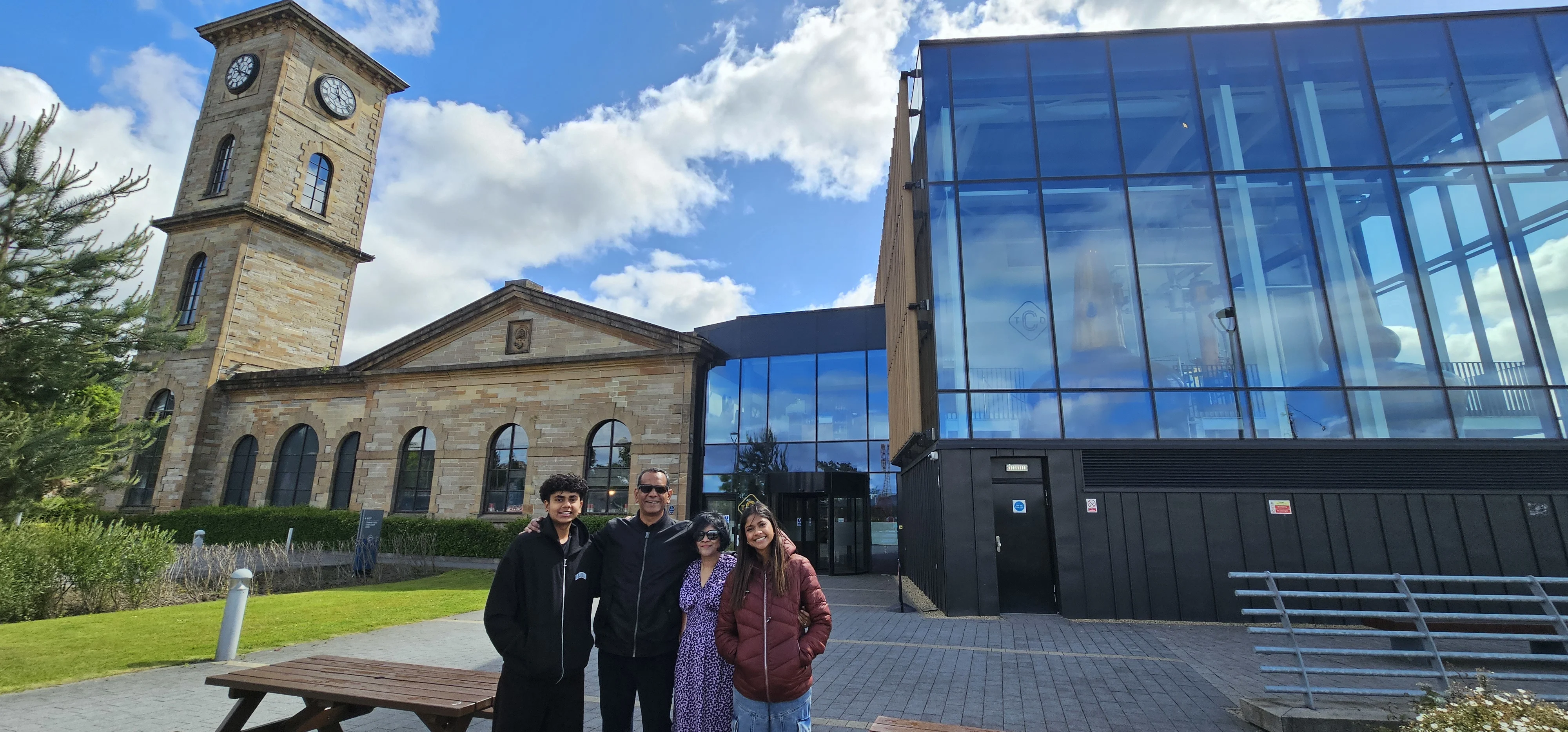 Four visitors standing outside historic stone church with modern glass extension building.