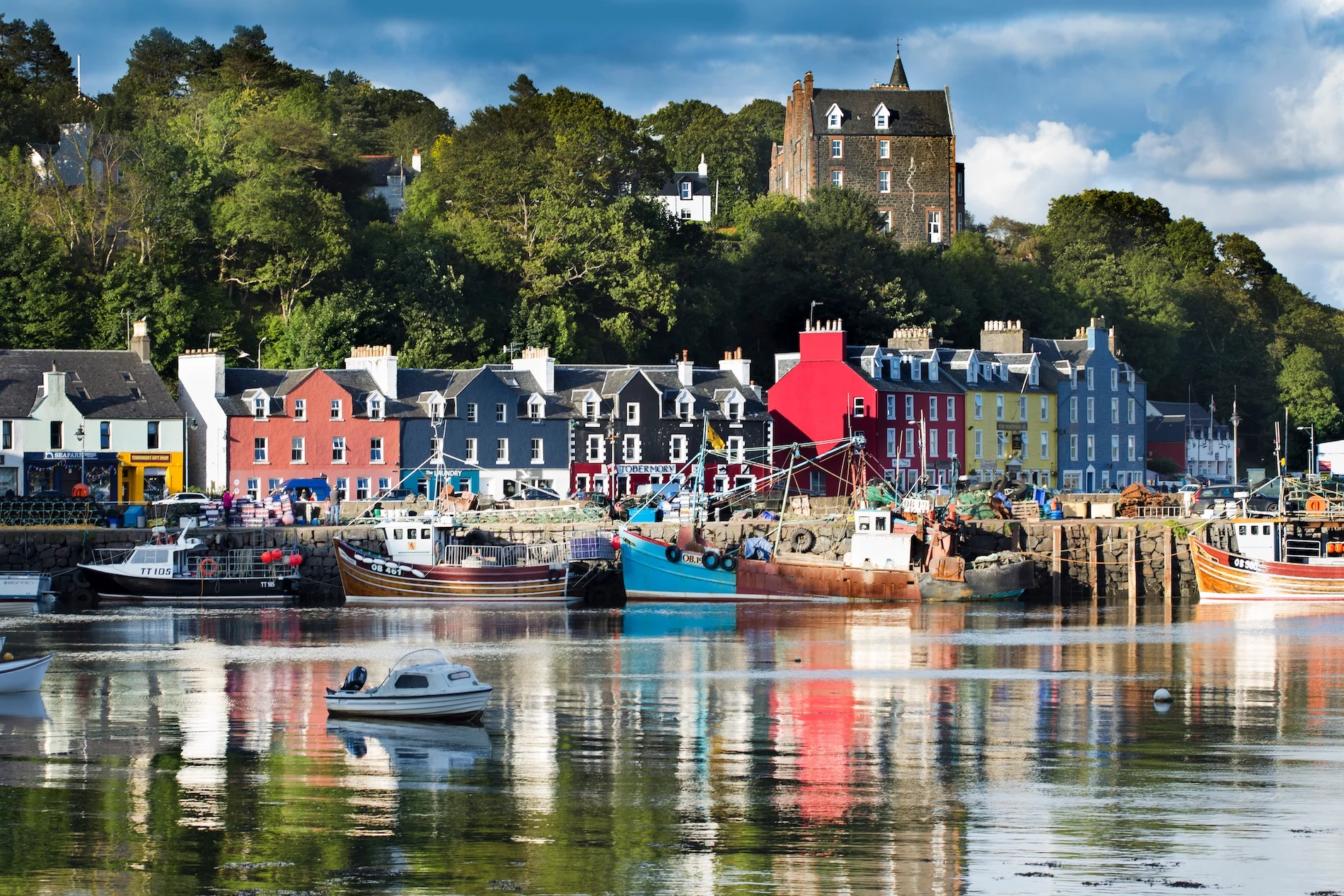 Colorful Scottish harbor village with boats and castle on hillside