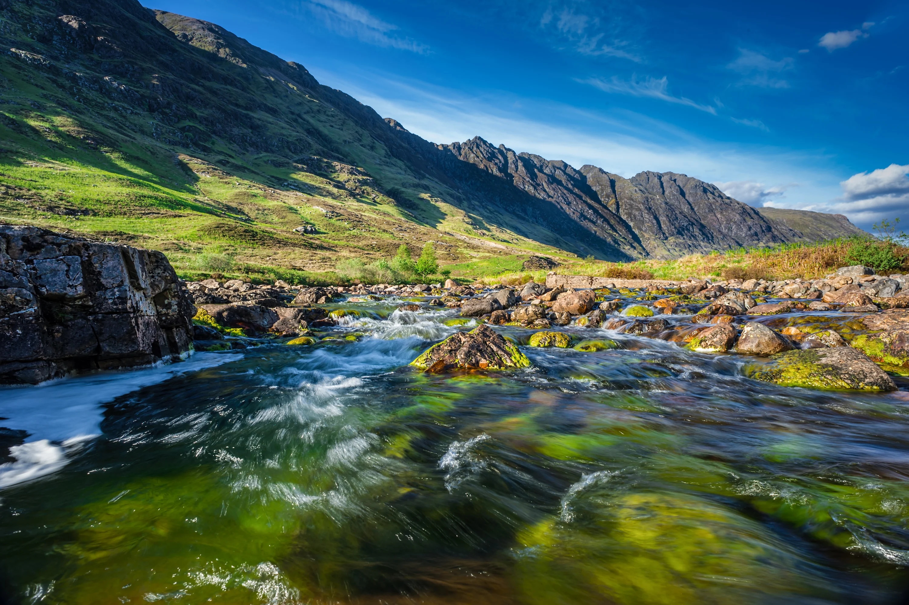 Mountain stream flowing through Scottish Highland valley with green hills