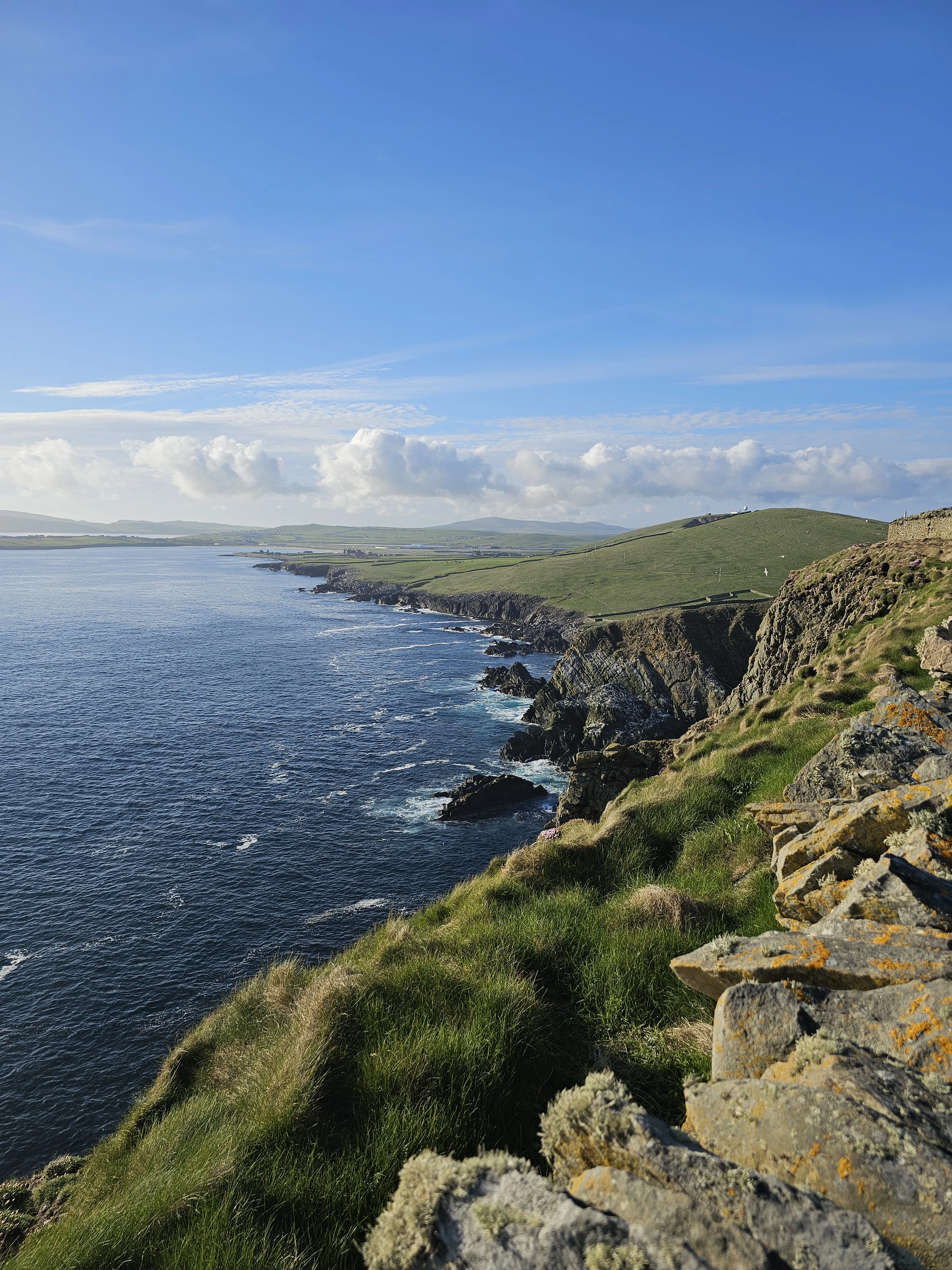 Dramatic Scottish coastal cliffs with green hills and rocky shoreline under blue sky